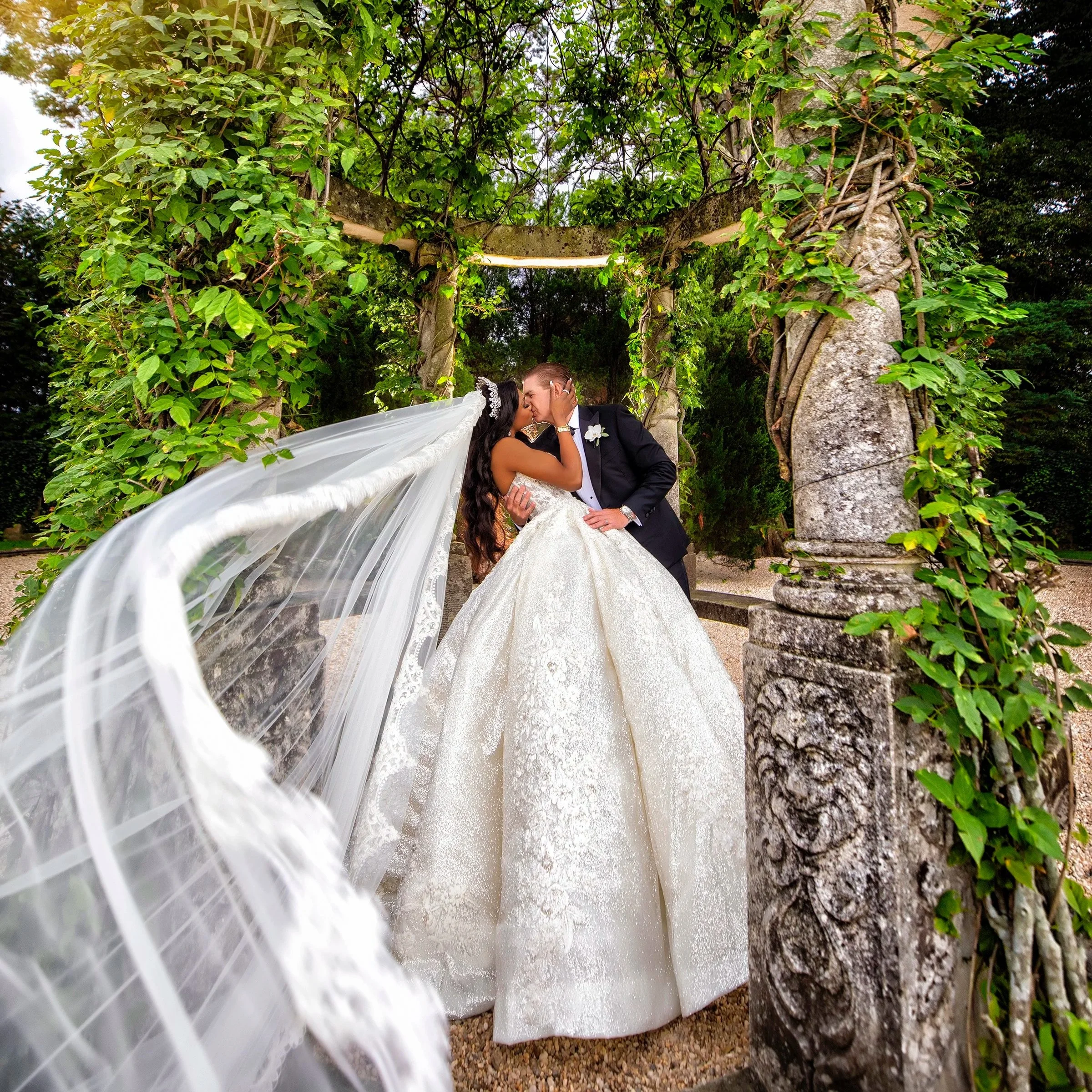Bride and Groom portrait with flowing veil in Oheka Castle’s original stone gazebo covered in wisteria vines