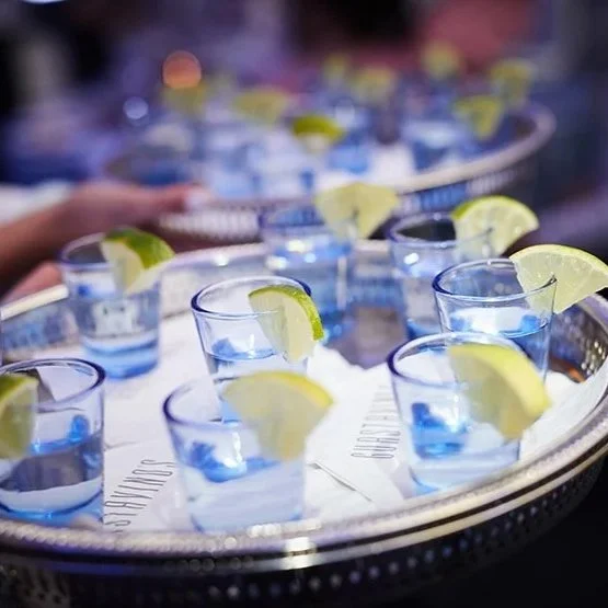 Tray of blue tequila shots, garnished with lemon wedges.
