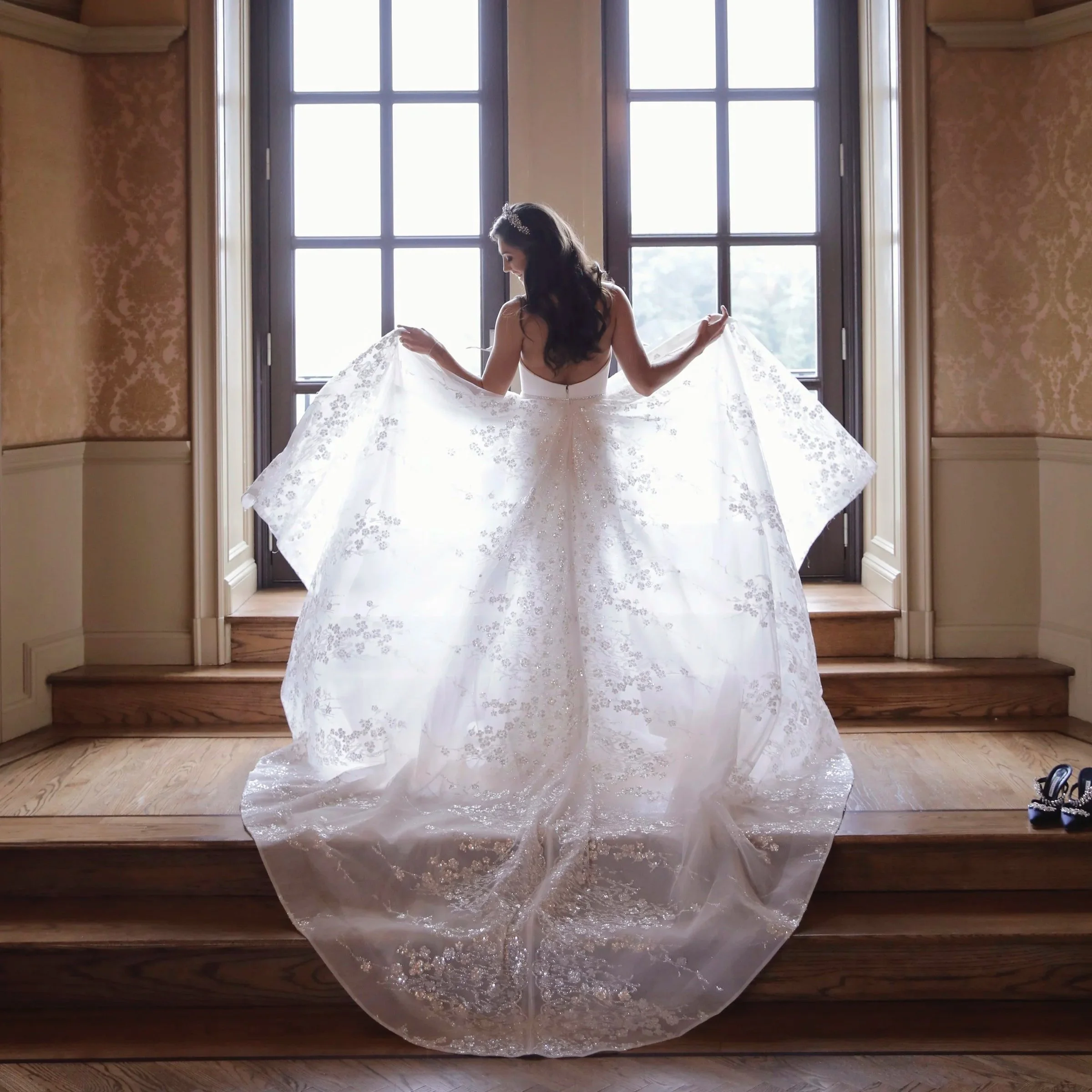 Bride holds up her gown in front of the balcony doors of the bridal suite at Oheka Castle 