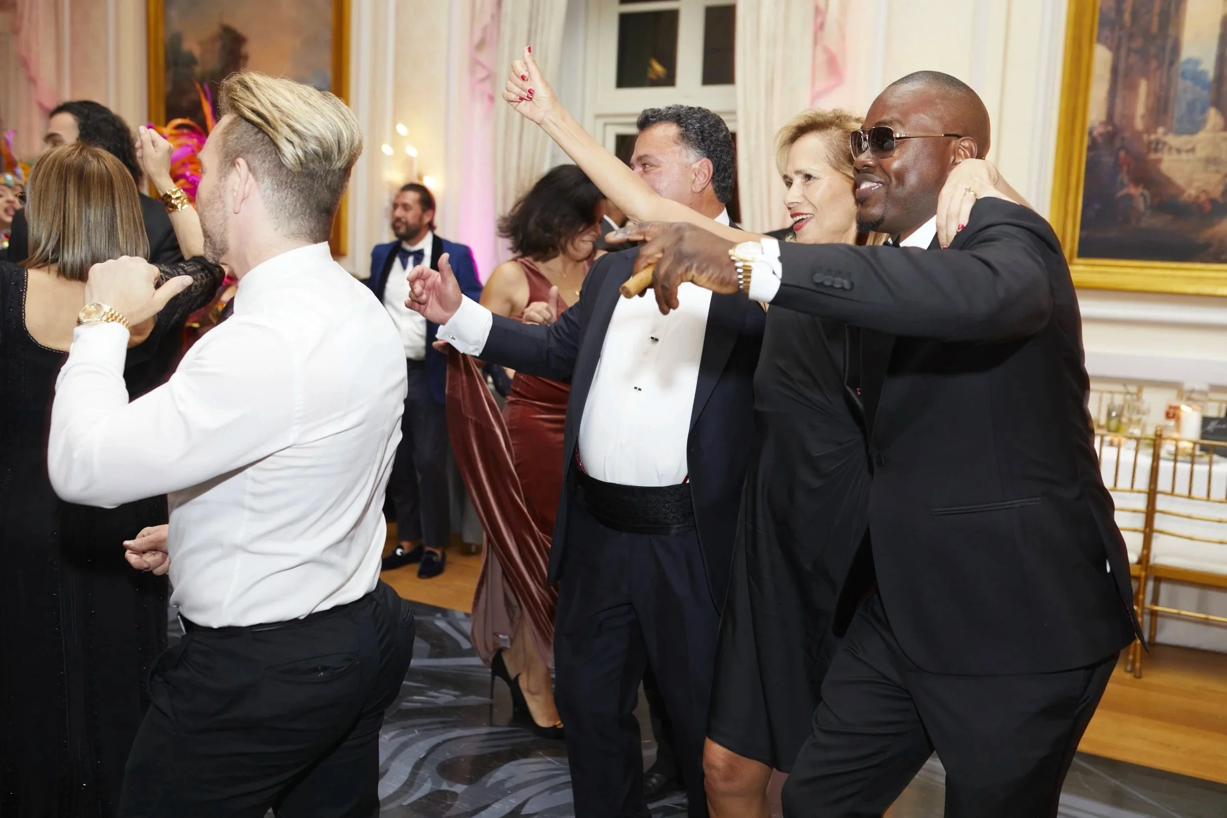 People dancing at a formal event in an elegant room with large framed paintings on the walls.