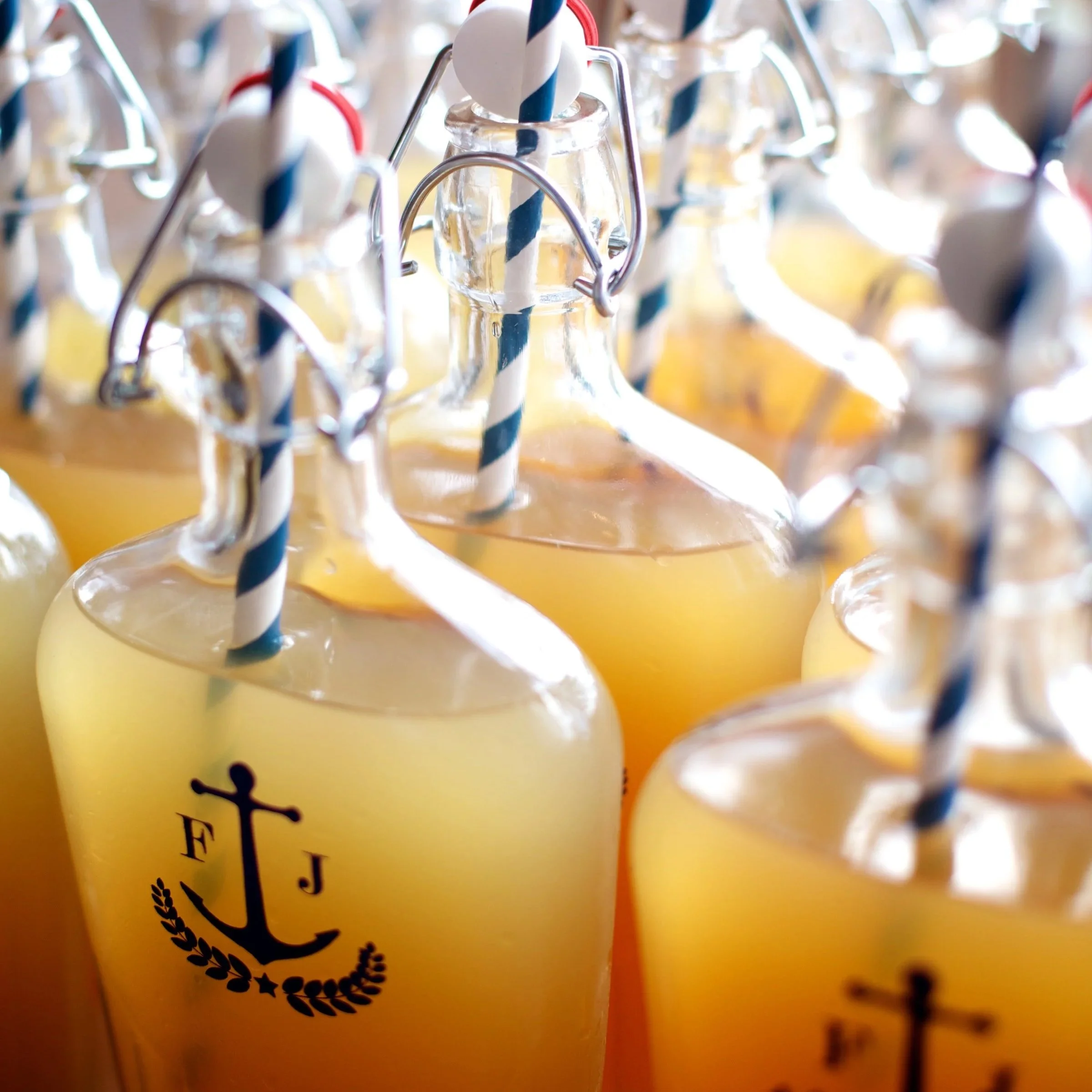 Multiple yellow beverage bottles with blue and white striped straws, some with metal caps and a crown logo, close-up shot.