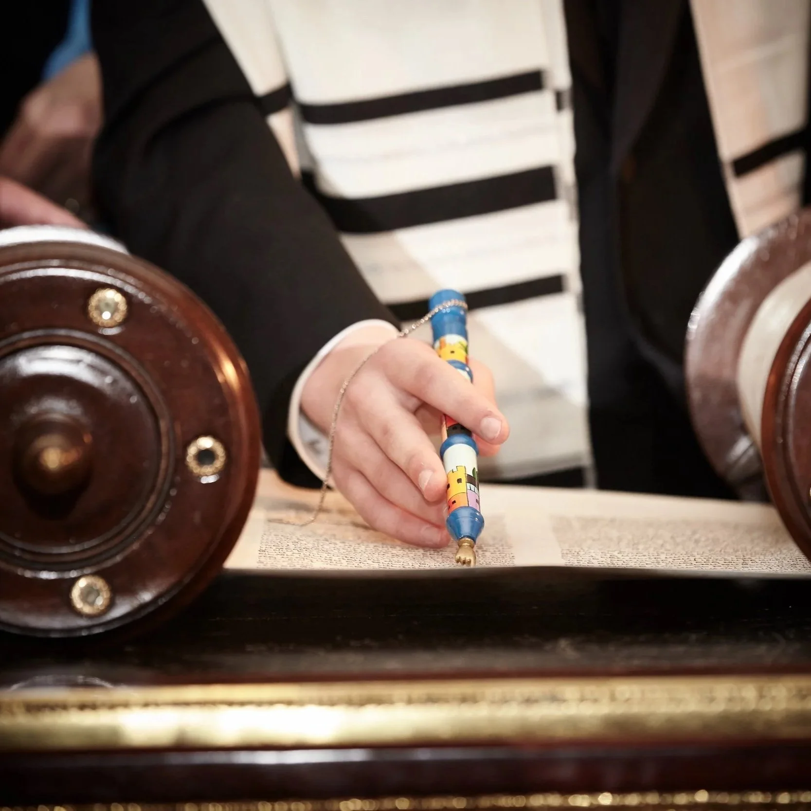 A person holding a colorful pen and writing on a piece of paper on a table, with a wooden object in the foreground and leather luggage in the background.