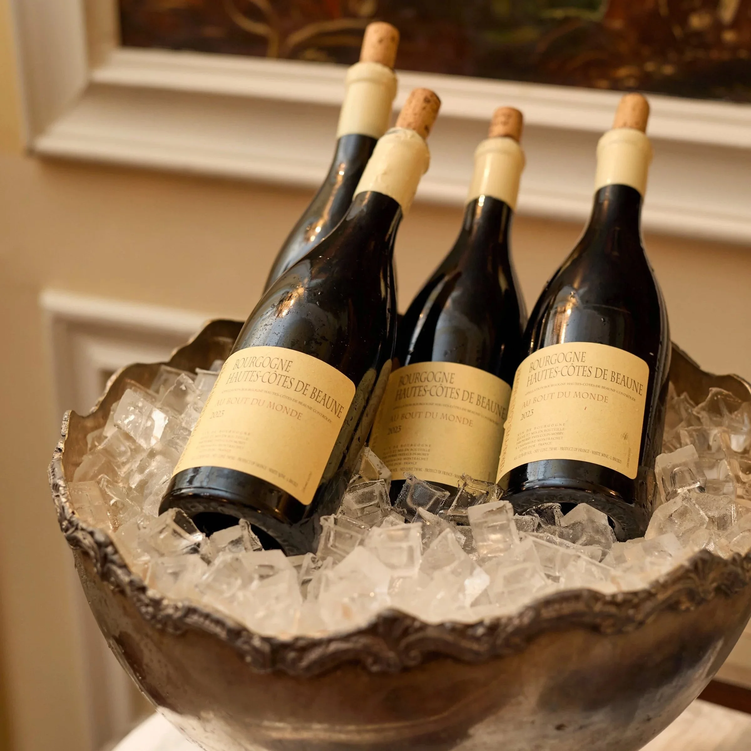 A metal ice bucket filled with ice cubes holding five bottles of Bourgogne Hautes-Côtes de Beaune wine with corks.
