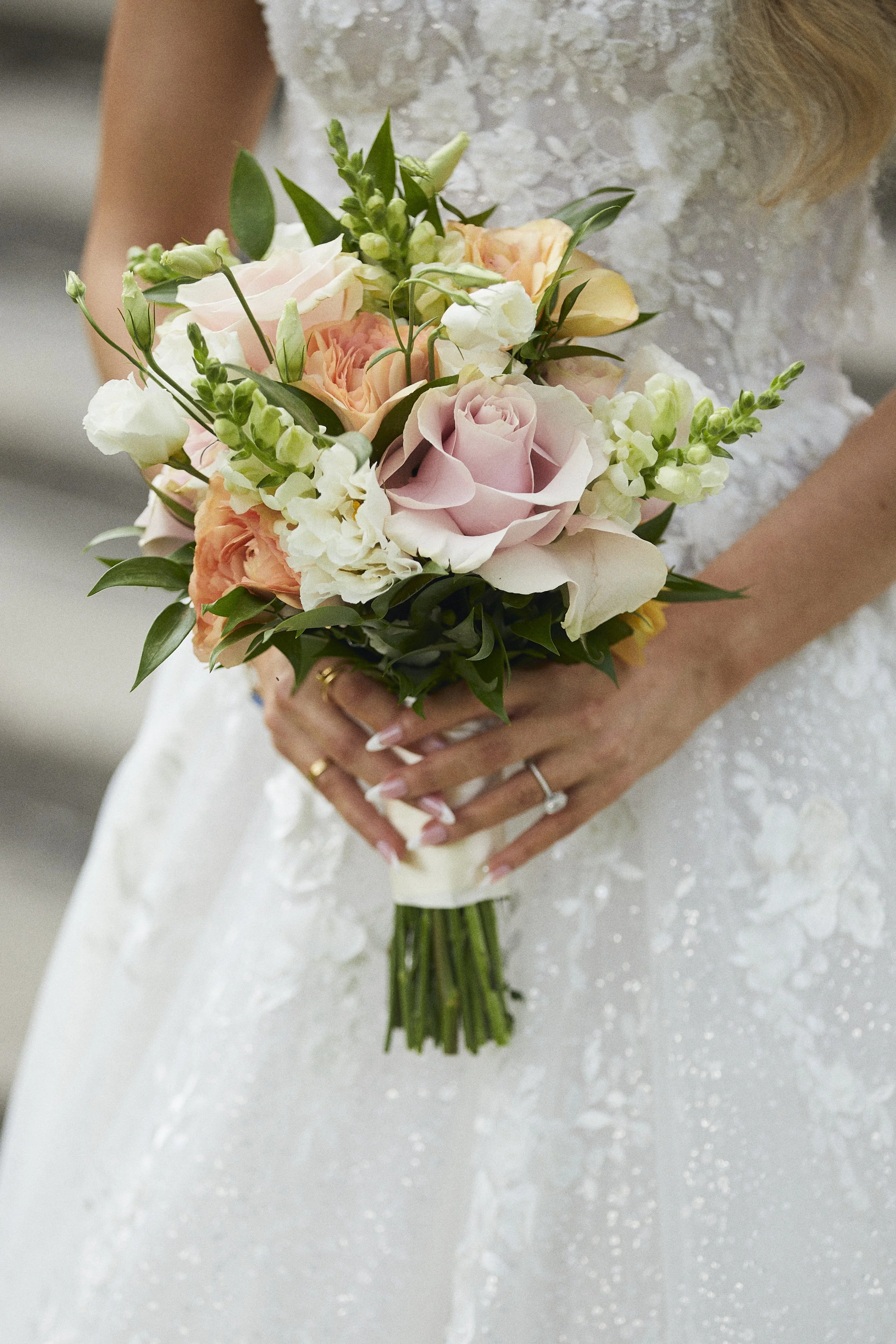 Bridal bouquet featuring blush, peach, and ivory flowers against a lace wedding gown