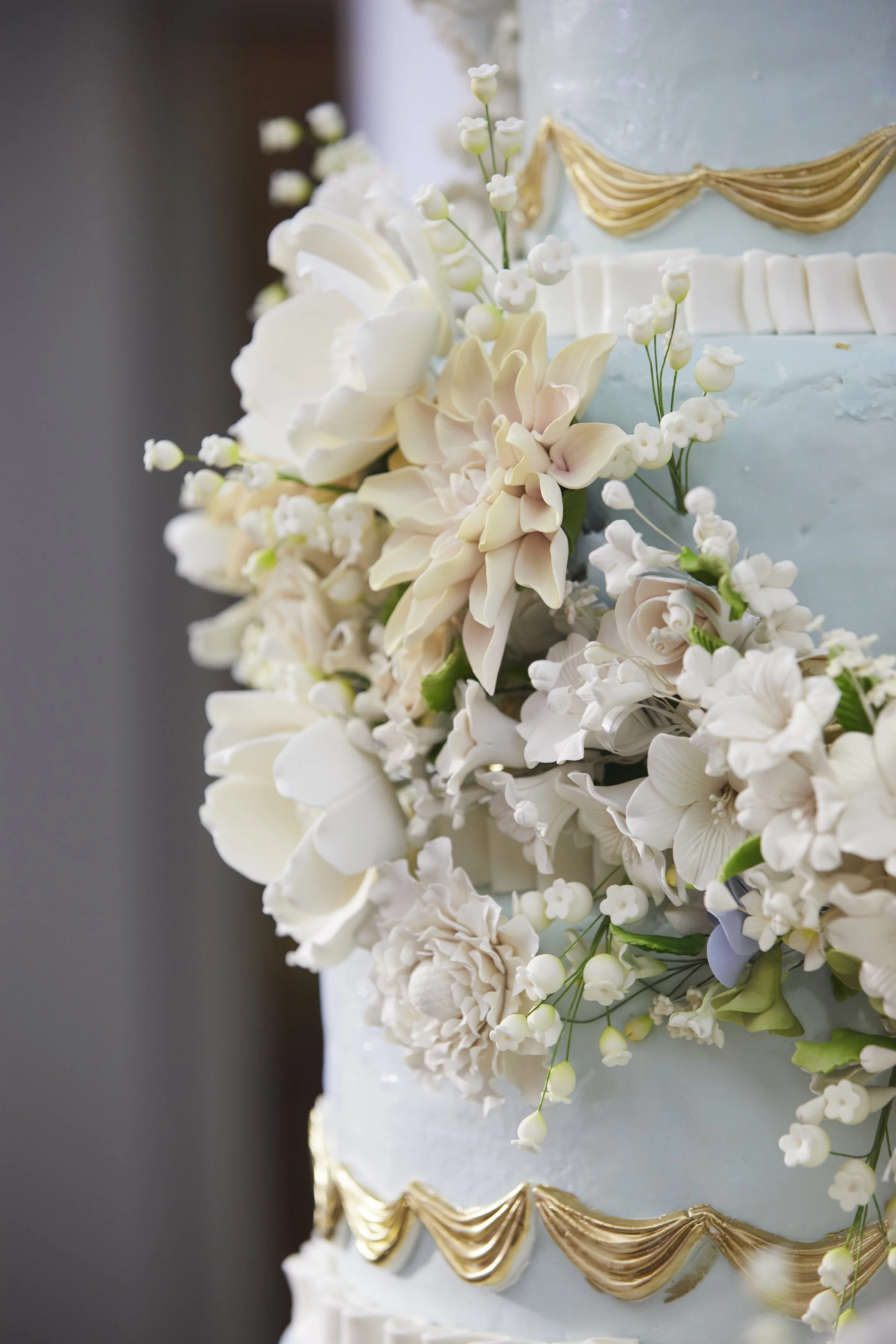 Sugar flowers on a soft blue wedding cake with gold accents.