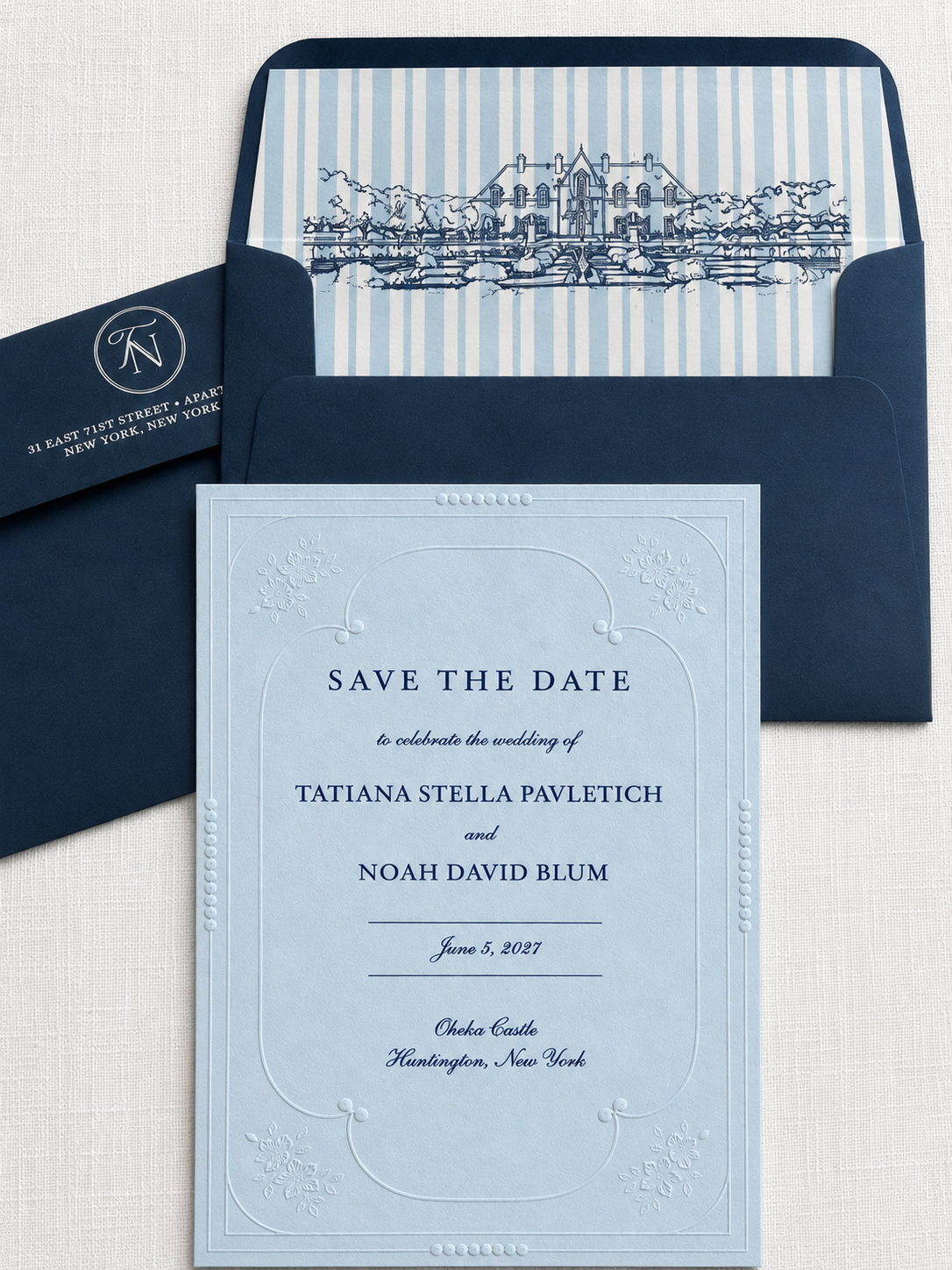 Save the date invitation in azure blue paper with embossed floral border details, navy blue ink and coordinating navy envelopes, featuring a blue-and-white striped envelope liner with a hand-drawn sketch of Oheka Castle on a white linen backdrop.