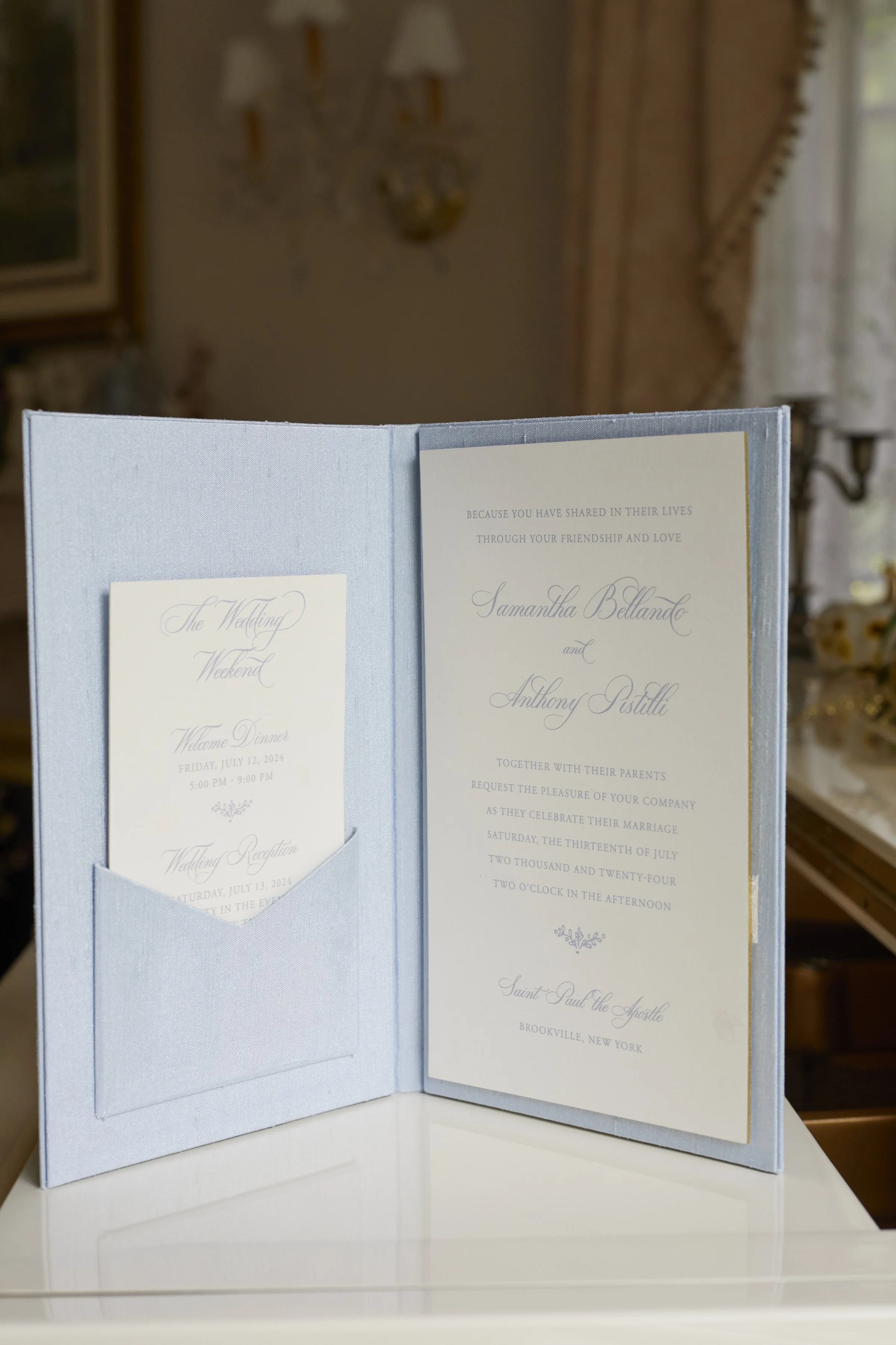 Samantha and Anthony’s custom wedding invitation suite displayed within a soft blue silk folio designed for the celebration at Oheka Castle.