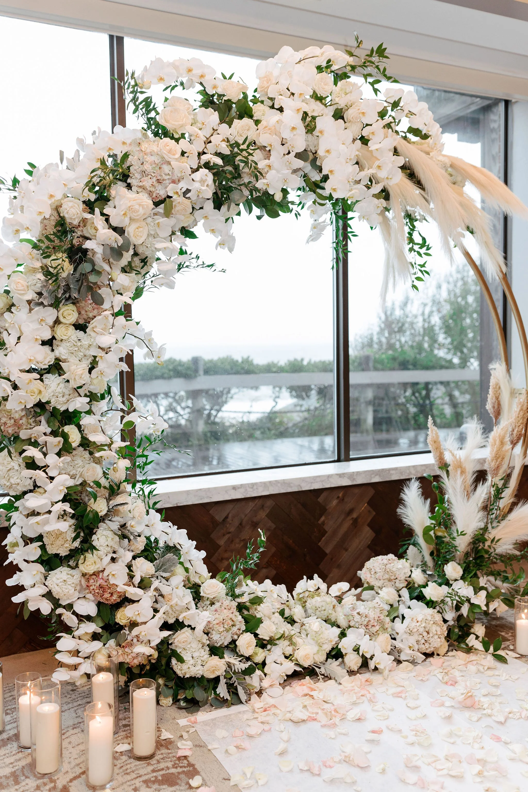 A sculptural floral installation framed the ceremony, where cascading orchids, garden roses, and soft greenery formed an organic arch against the ocean beyond—an ethereal setting that felt both elevated and intimately connected to the coast at Gurney