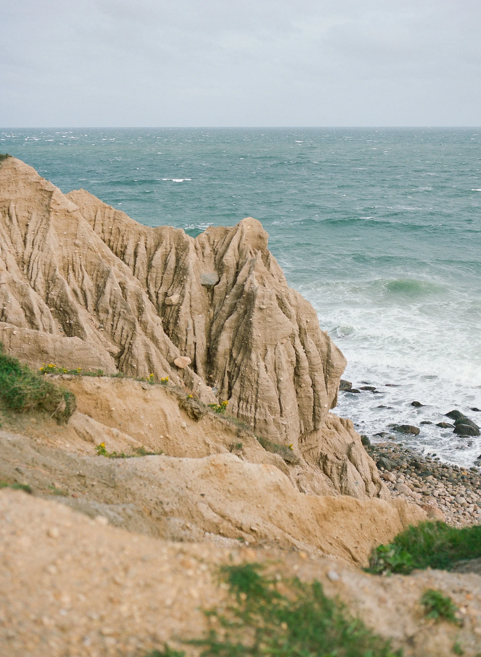 Cliffs with eroded layers overlooking a turbulent ocean under an overcast sky.
