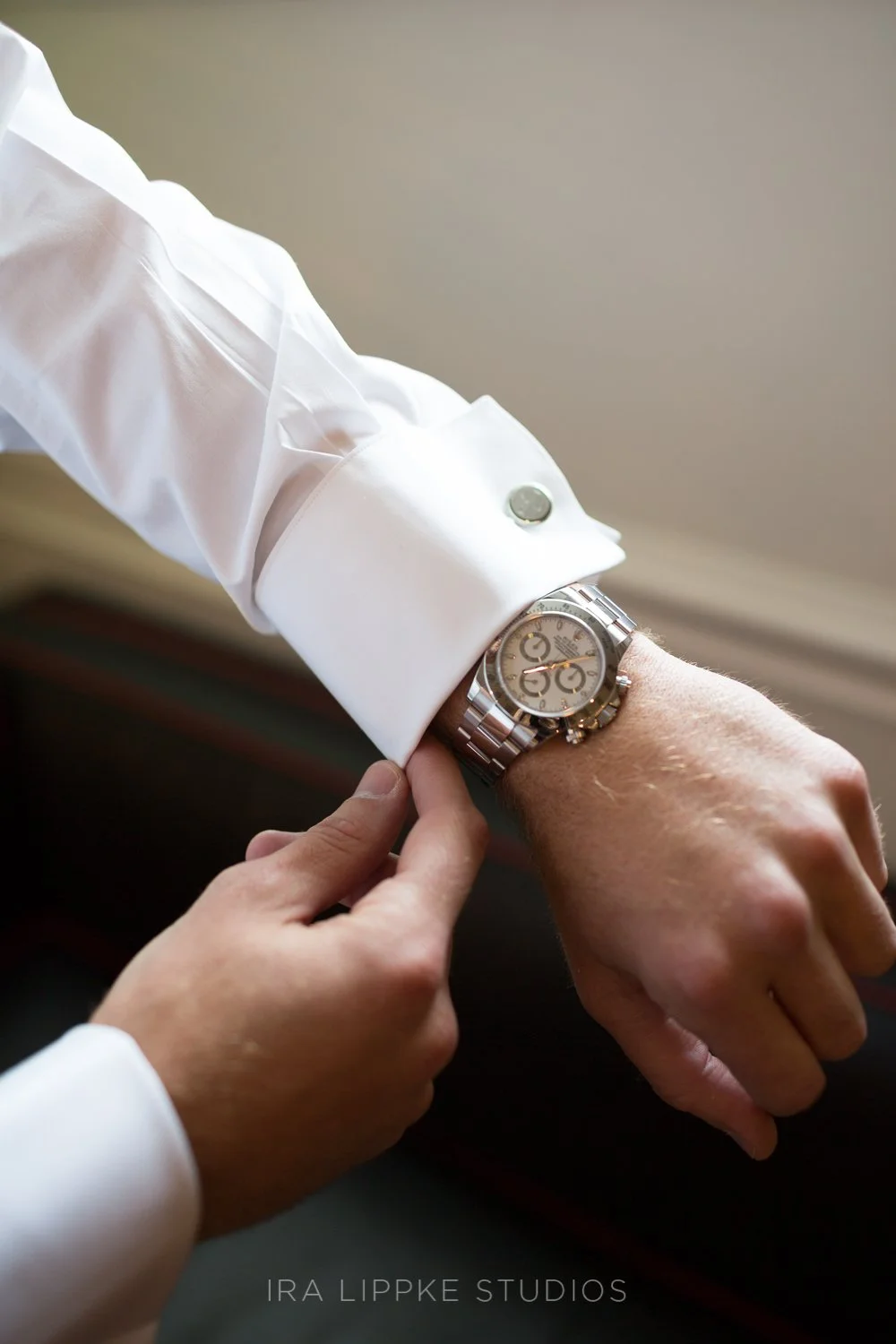 The groom adjusts his cufflinks and watch, a quiet moment of anticipation before seeing his bride.