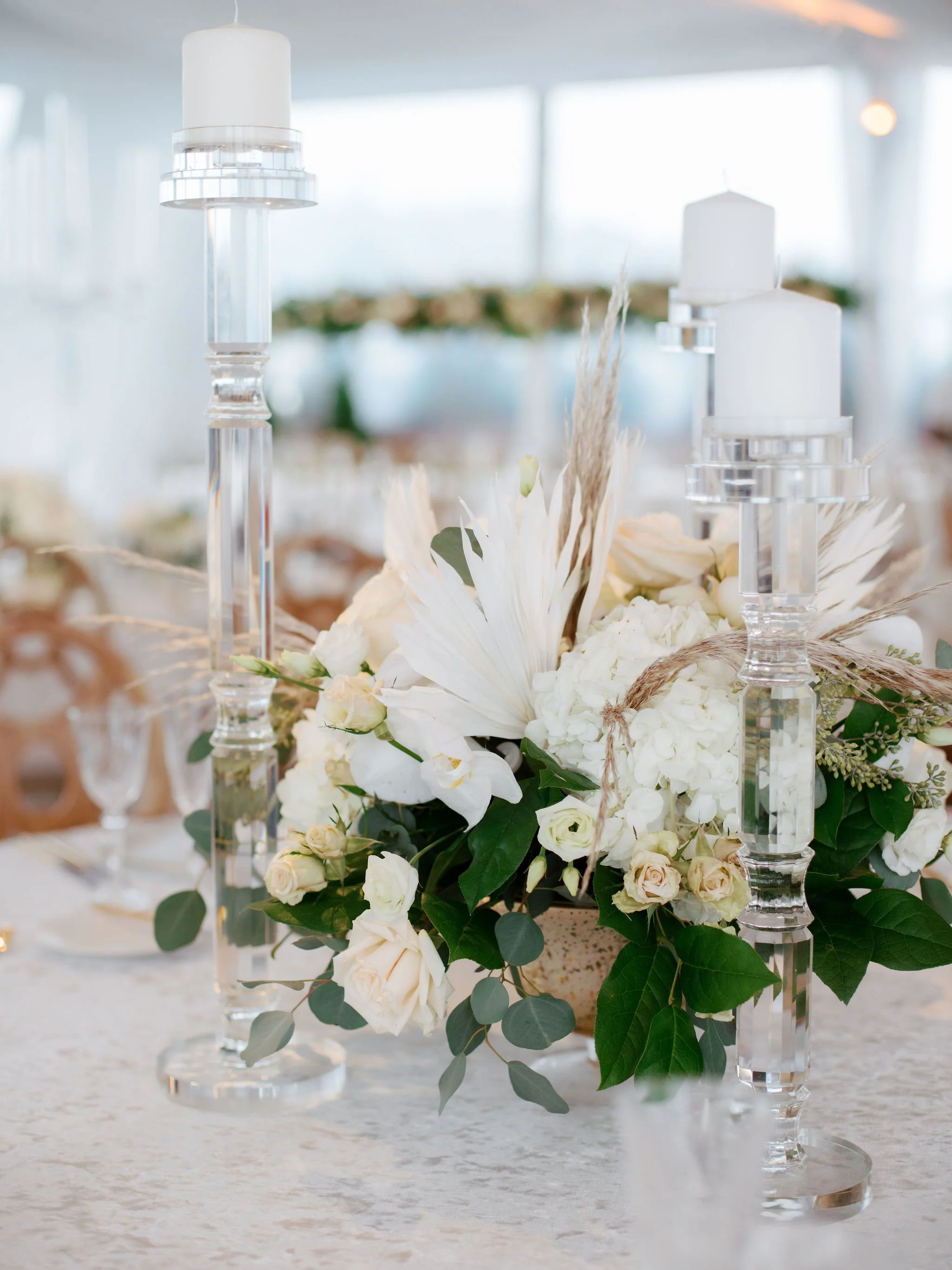 Elegant floral centerpiece with white roses, greenery, and candle holders on a table at a formal event.