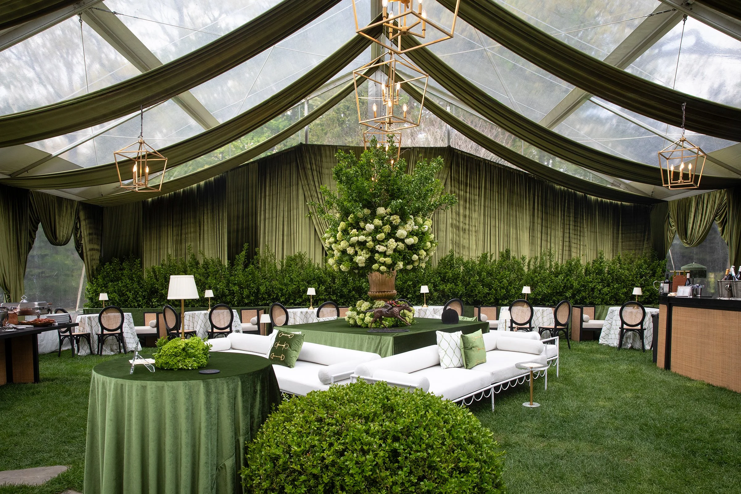 A custom tented lounge and dining space designed for the Kentucky Derby celebration featuring layered green textures, equestrian-inspired details, and garden-style seating arrangements.