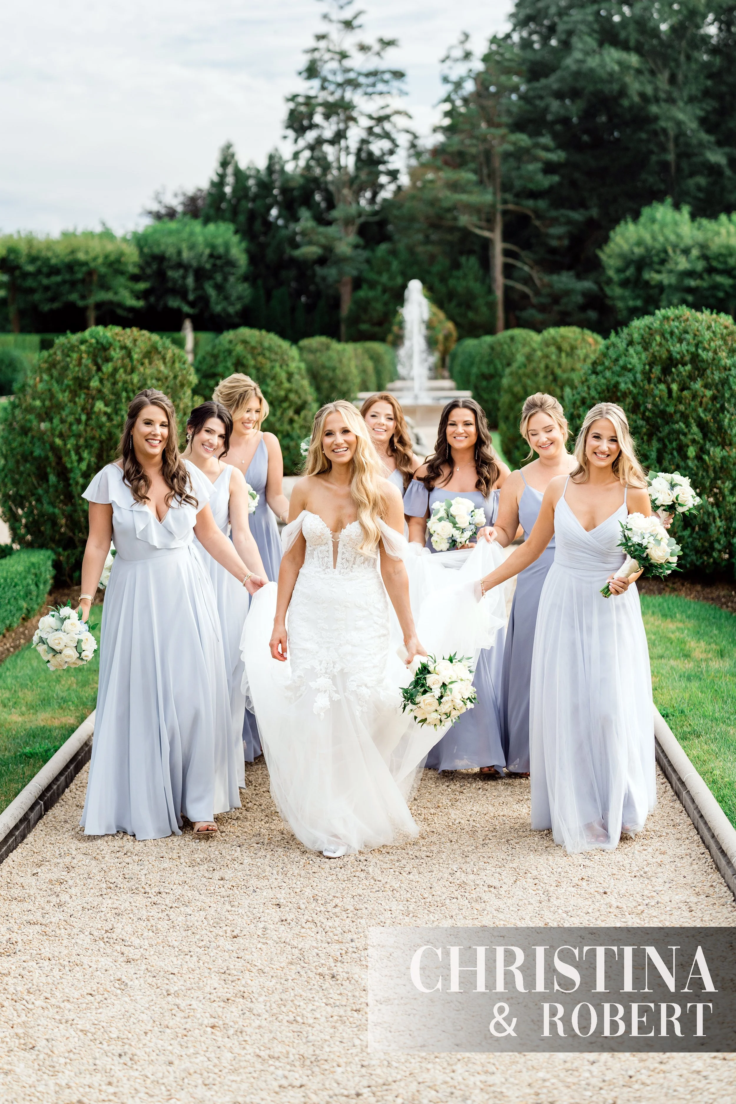 Bride and her bridesmaids in light blue gowns walking in the water gardens at Oheka Castle.