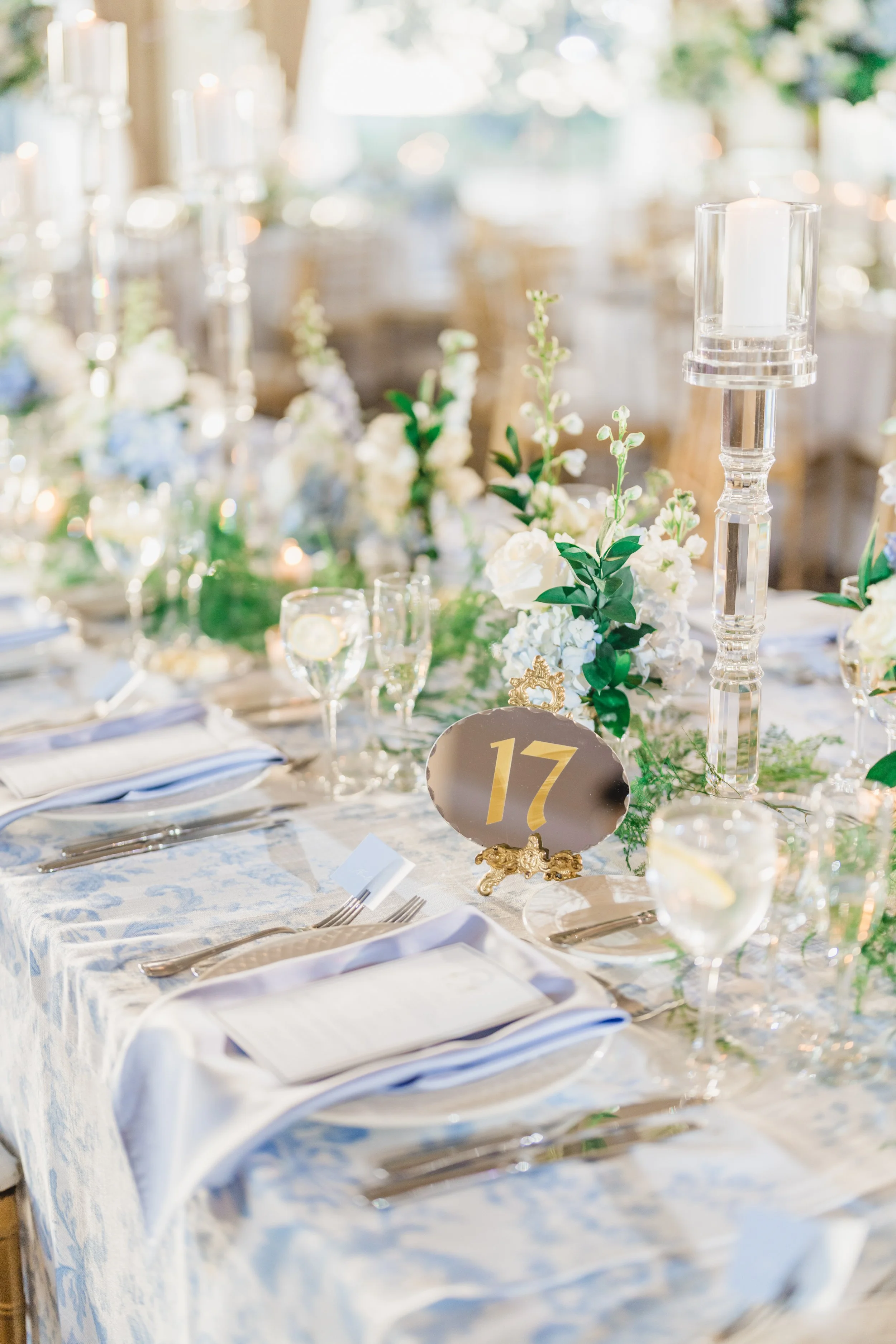 Table number 17 displayed on mirrored stand with blue and white floral wedding decor
