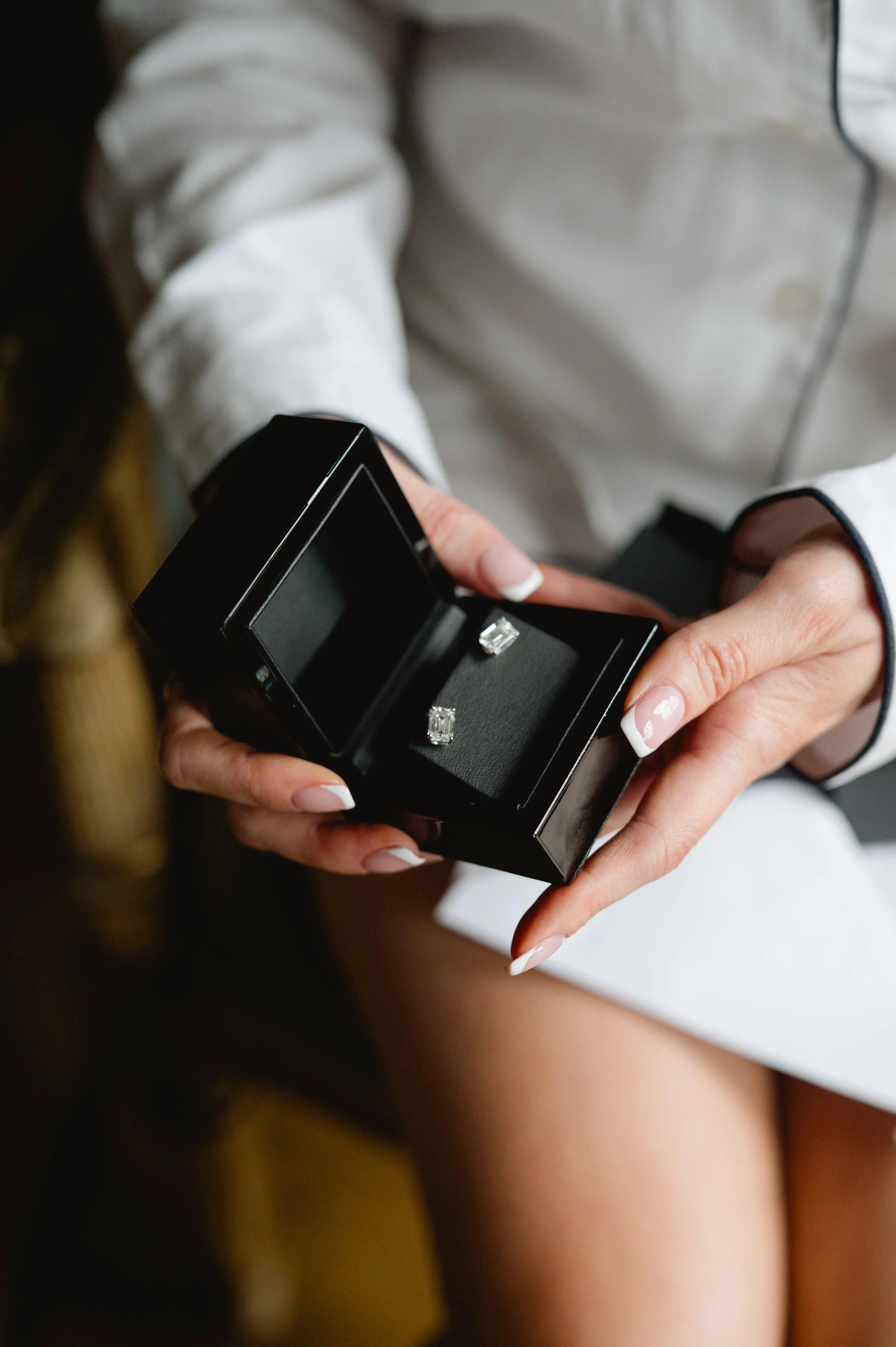 A person holding an open black jewelry box with two diamond rings inside.