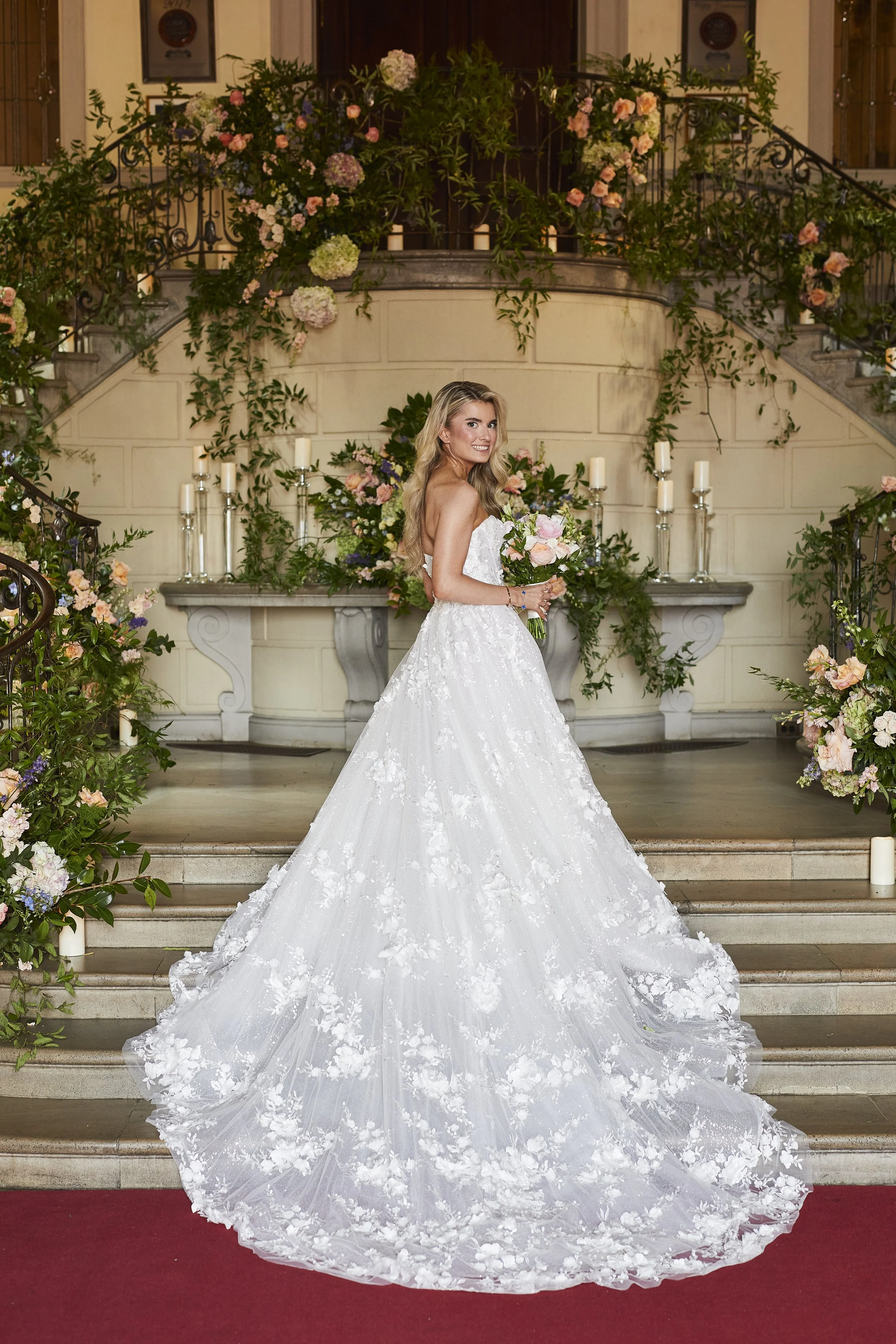 Bride standing on Oheka Castle staircase surrounded by lush floral installations