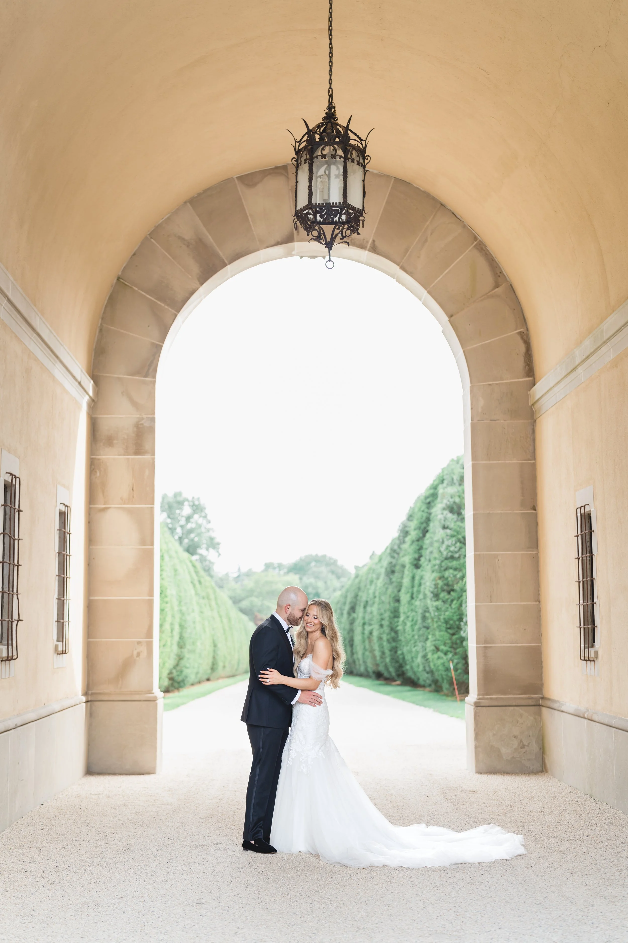 Bride and groom embracing under grand archway at Oheka Castle estate