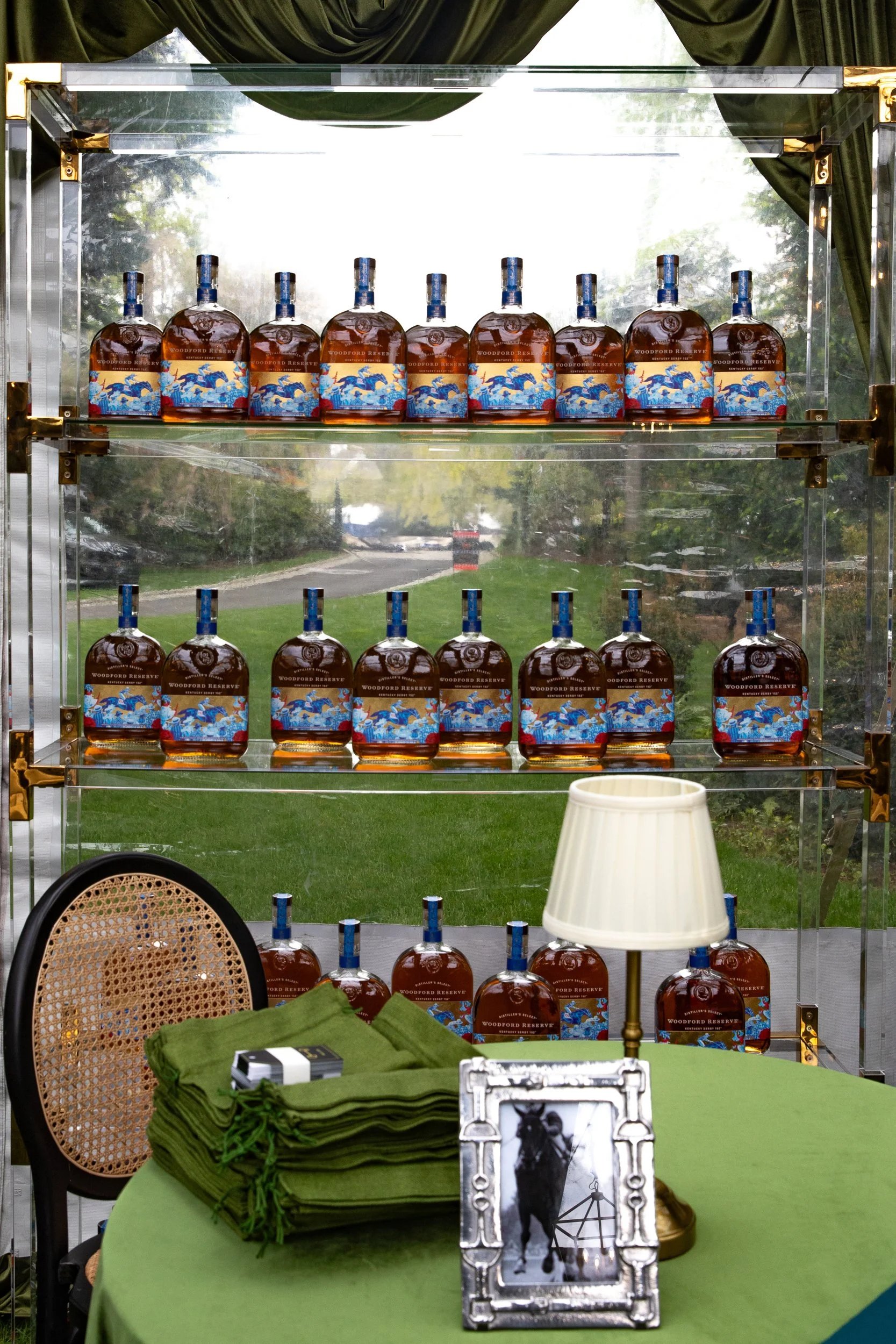 Guest gifts of Woodford Reserve Bourbon bottles featuring the 2026 Kentucky Derby artwork, custom engraved on-site and packaged in green linen bags with black and gold name tags for guests to take home.
