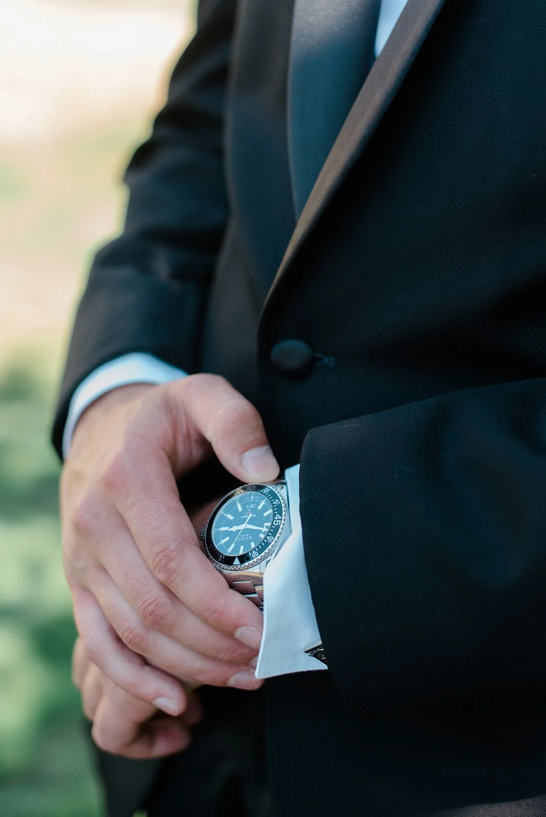 Close-up of a person wearing a black suit adjusting their silver watch.
