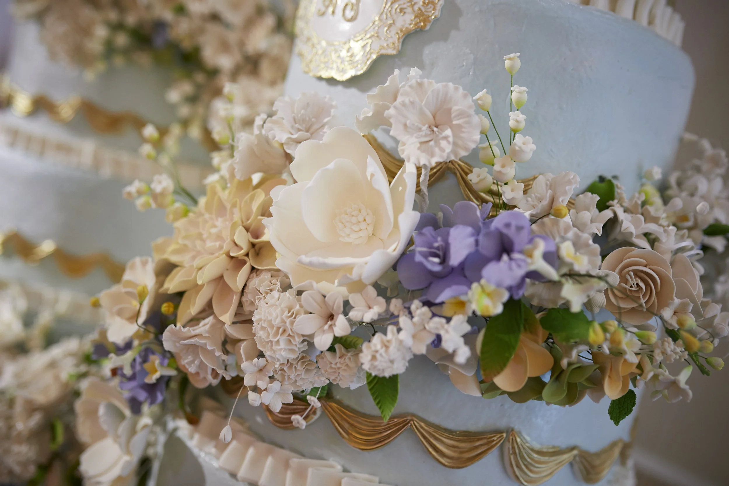 A close-up of Samantha and Anthony’s wedding cake adorned with handcrafted sugar flowers, soft pastel tones, and intricate gold detailing.