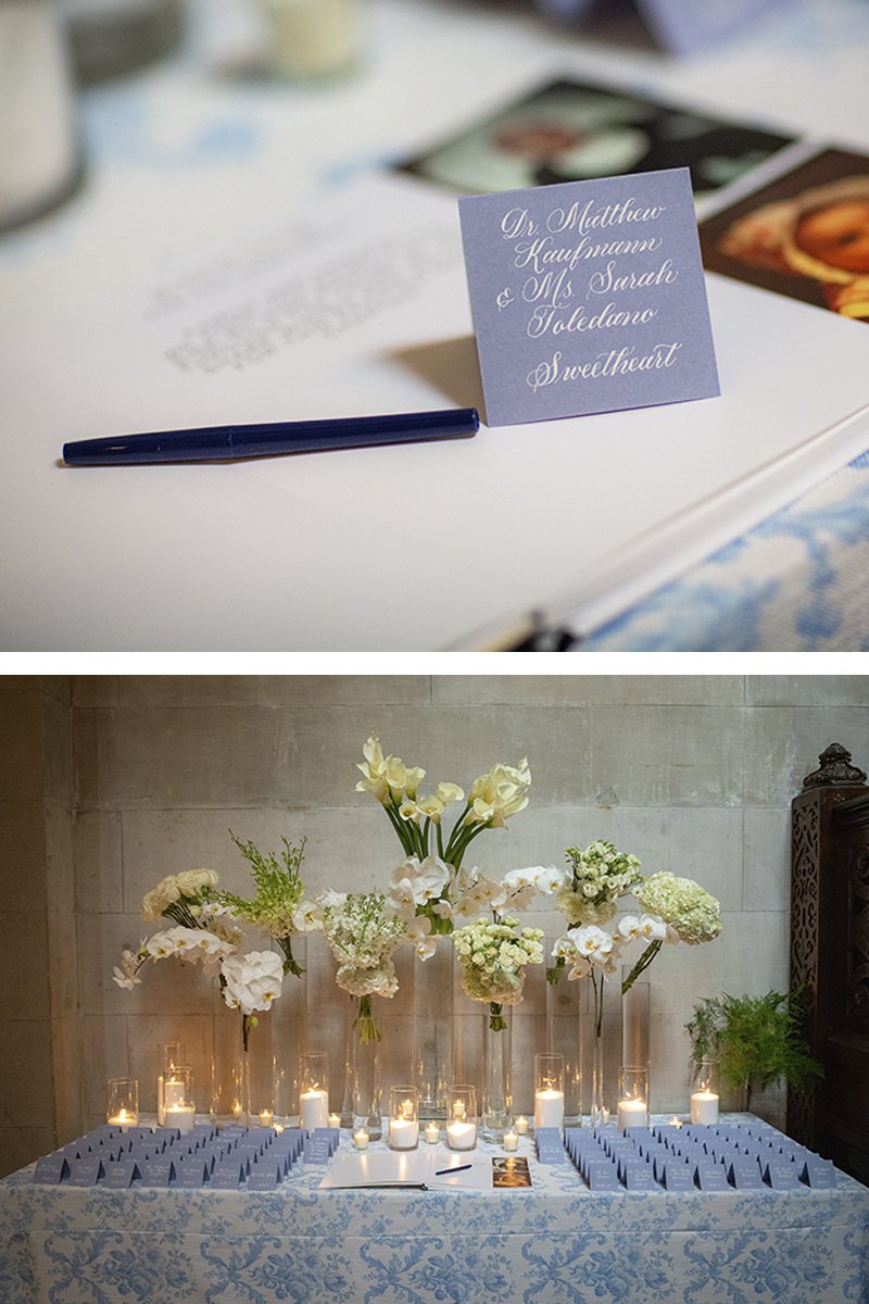 Escort card table with blue calligraphy cards, candles, and white floral arrangements at wedding reception