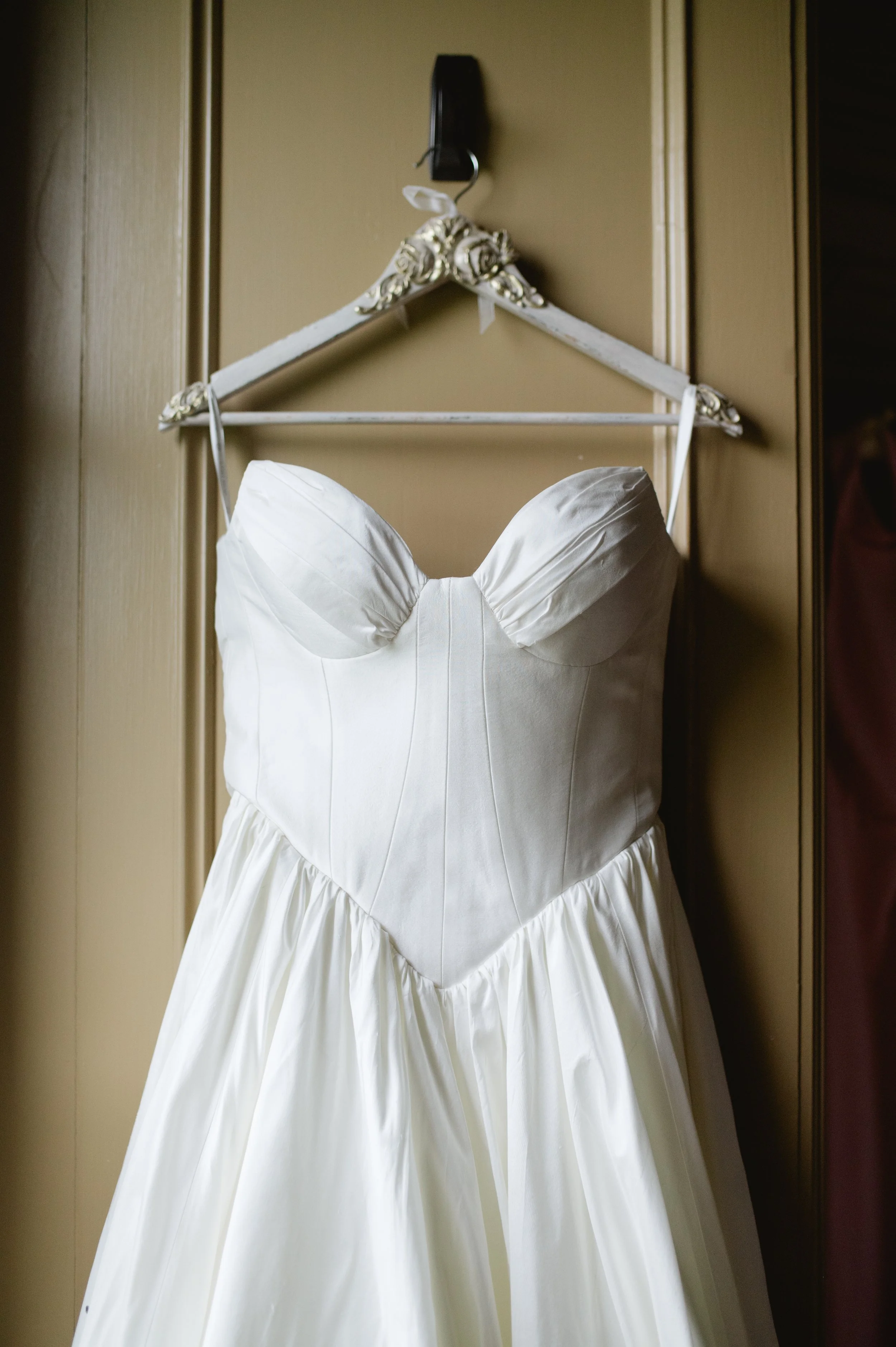 A white wedding dress hanging on an ornate hanger on a beige closet door.