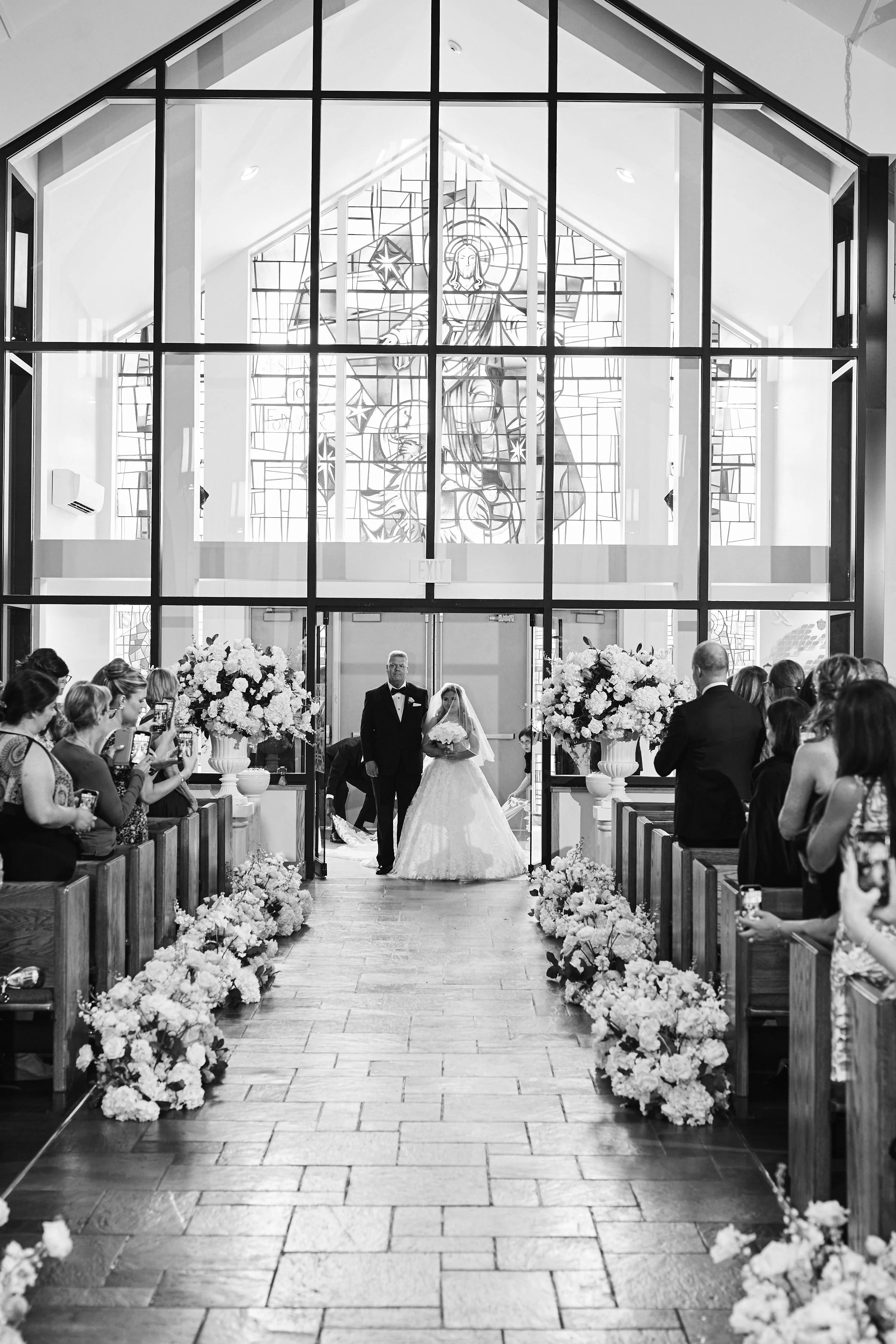 Samantha being escorted down the aisle by her father inside the grand church ceremony adorned with lush white florals and candlelit arrangements.