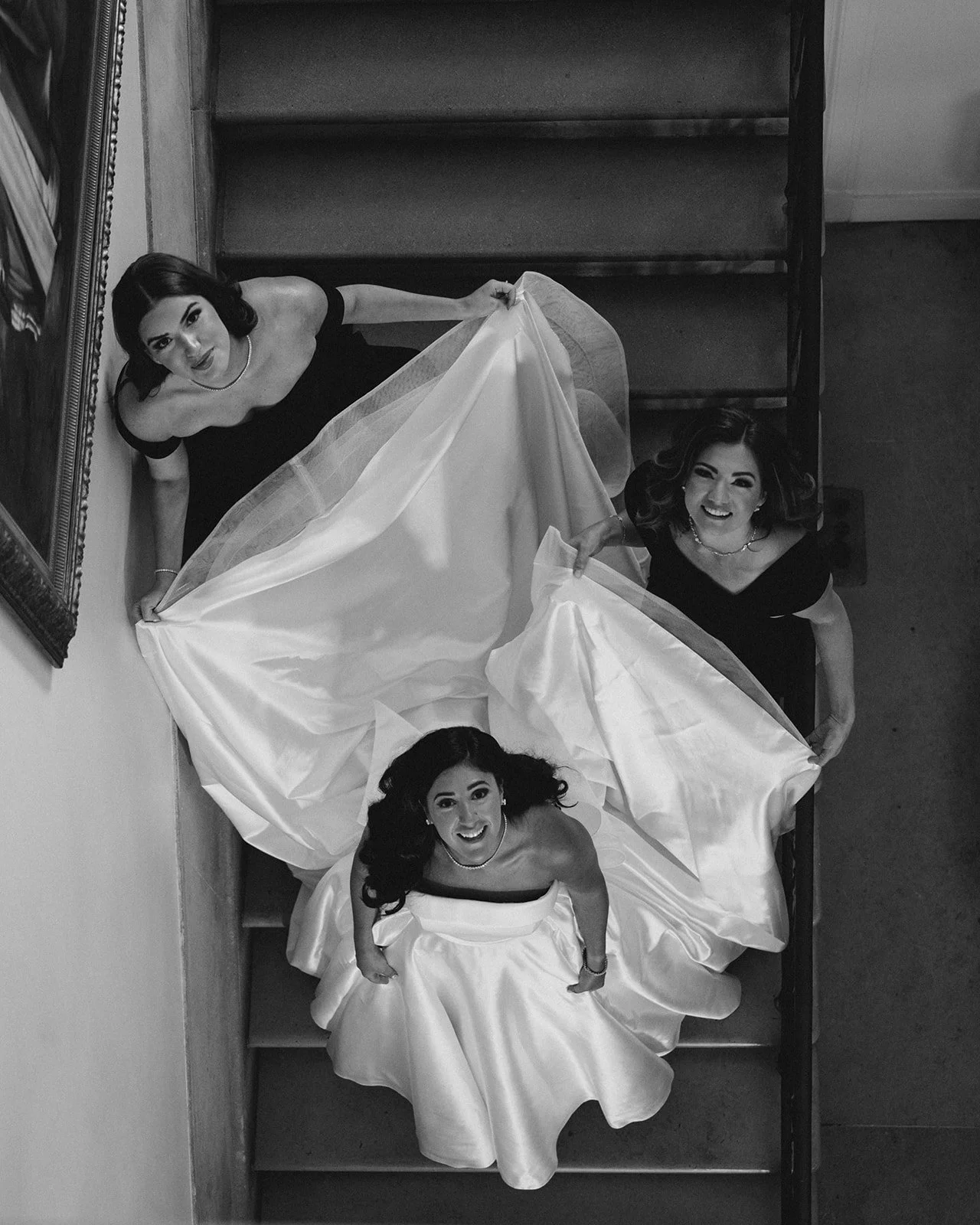 Black and white photo of three women in dresses lying on what appears to be a staircase, looking up at the camera and smiling.