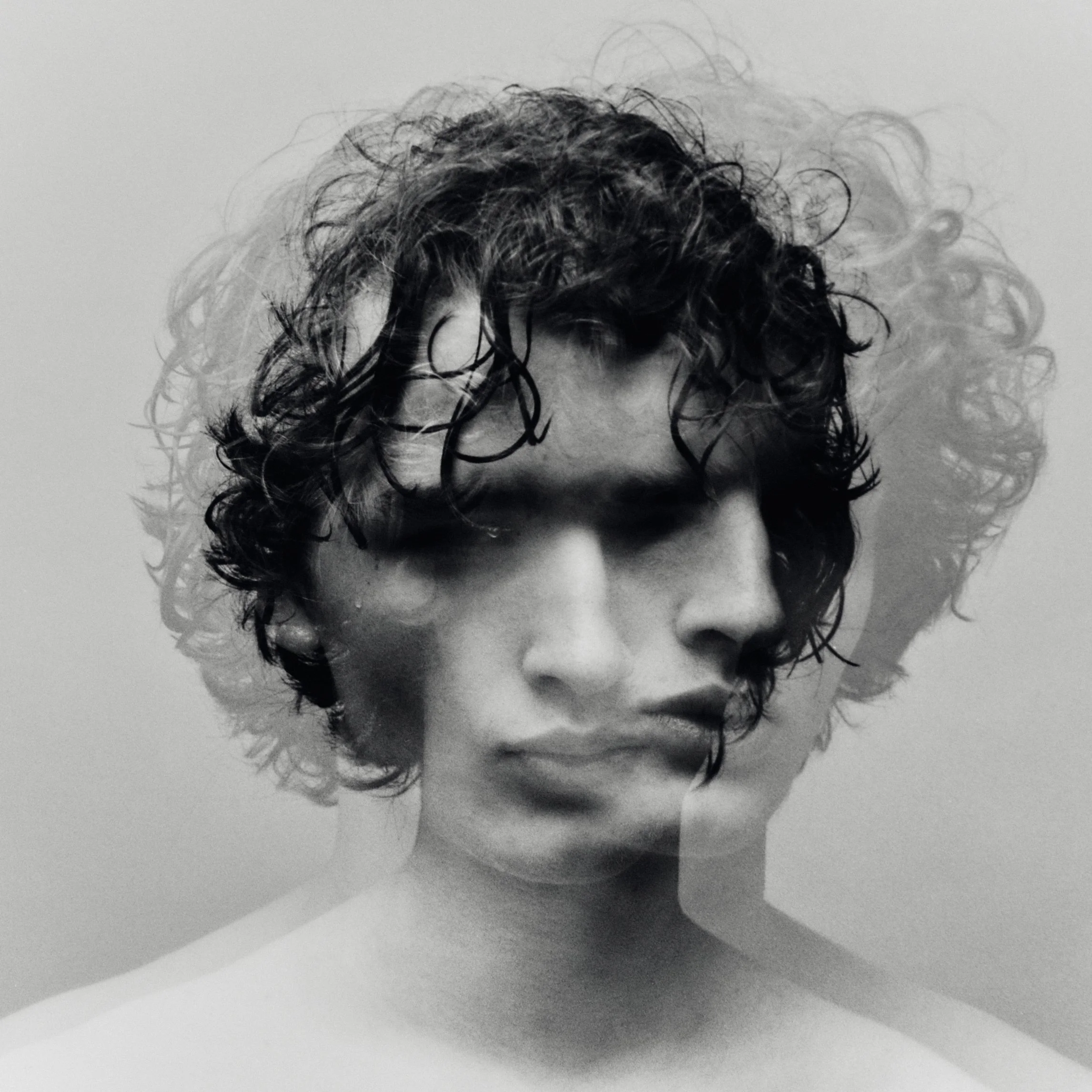 Black and white double exposure photograph of a woman's face with curly hair.