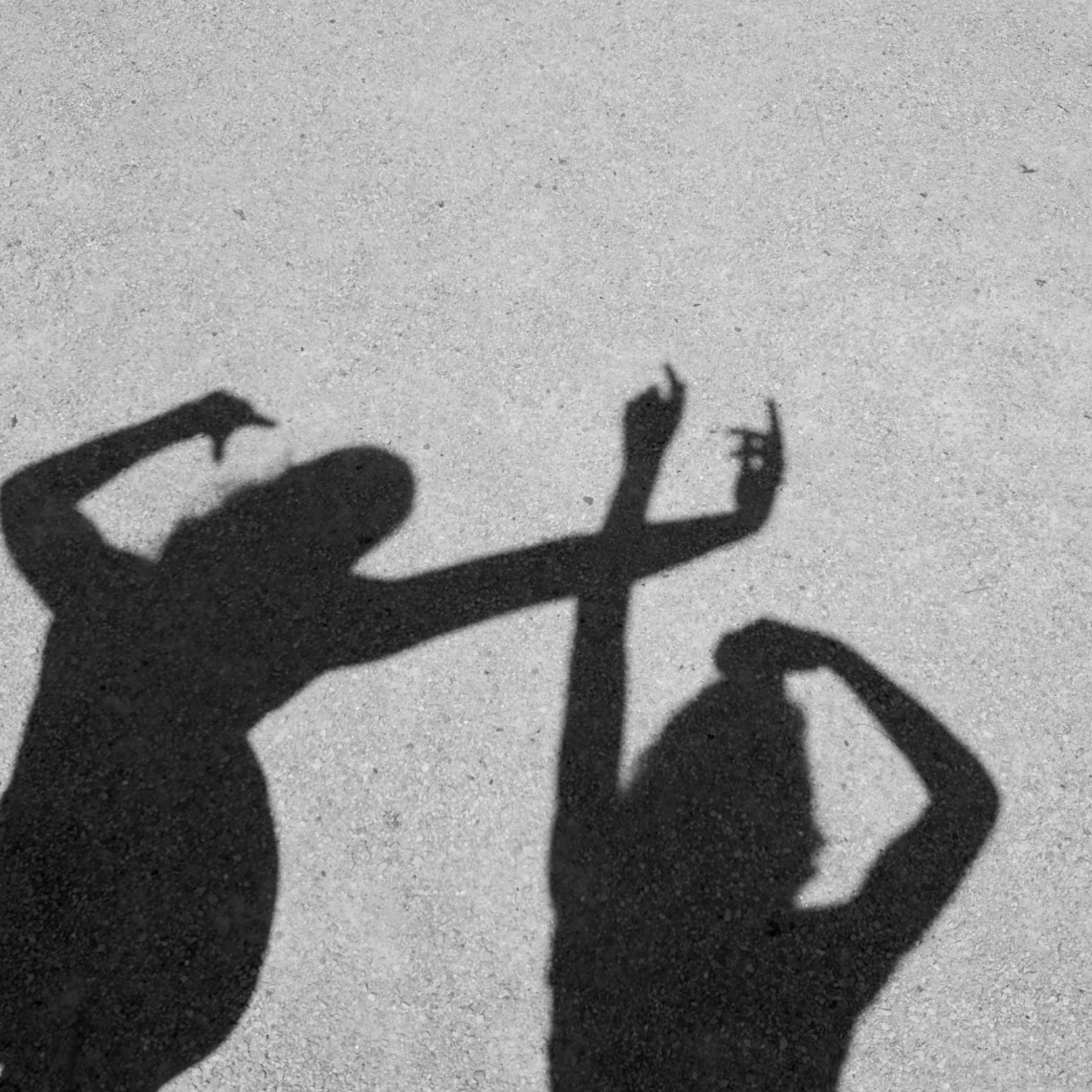 Shadow of two children playing and pointing at each other on a sandy surface with small pebbles.