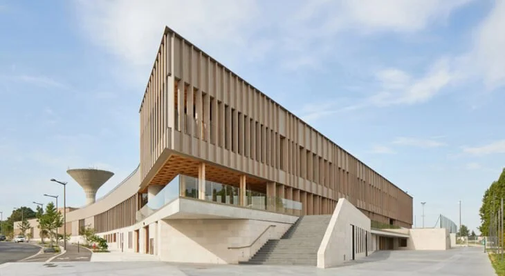 Un bâtiment moderne avec une façade en bois et des escaliers extérieurs, sous un ciel bleu avec quelques nuages.