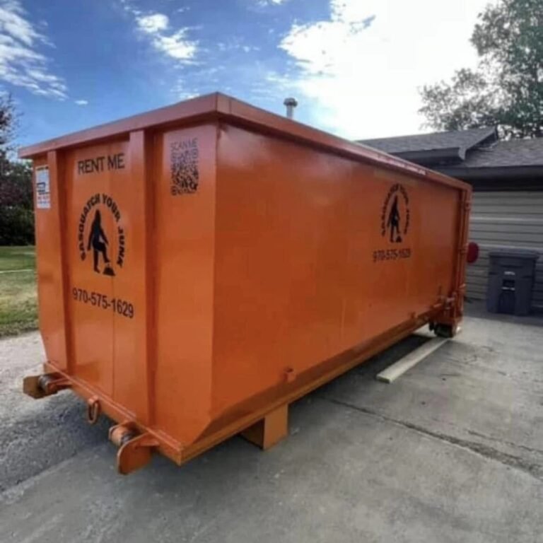 Large orange dumpster on a driveway, with a sasquatch logo crushing junk and a phone number. There is a QR code on one side.
