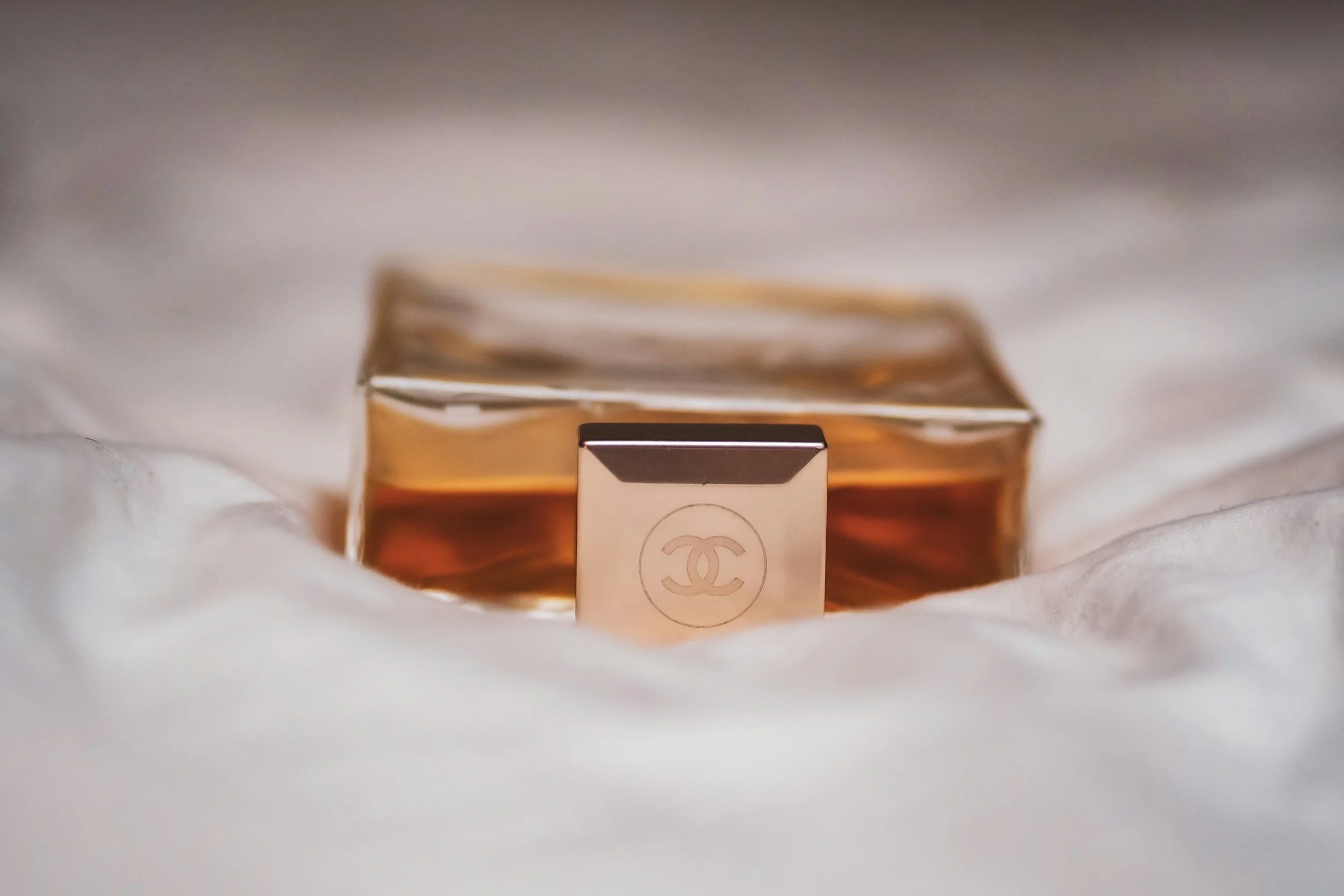 A small Chanel perfume bottle with a white cap and the Chanel logo on the front, in front of a stack of books, on a white surface.