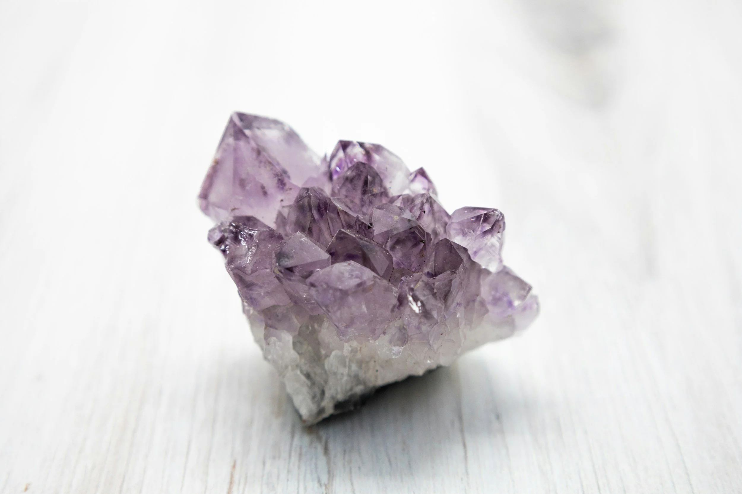 Purple amethyst crystal cluster on white wooden surface.