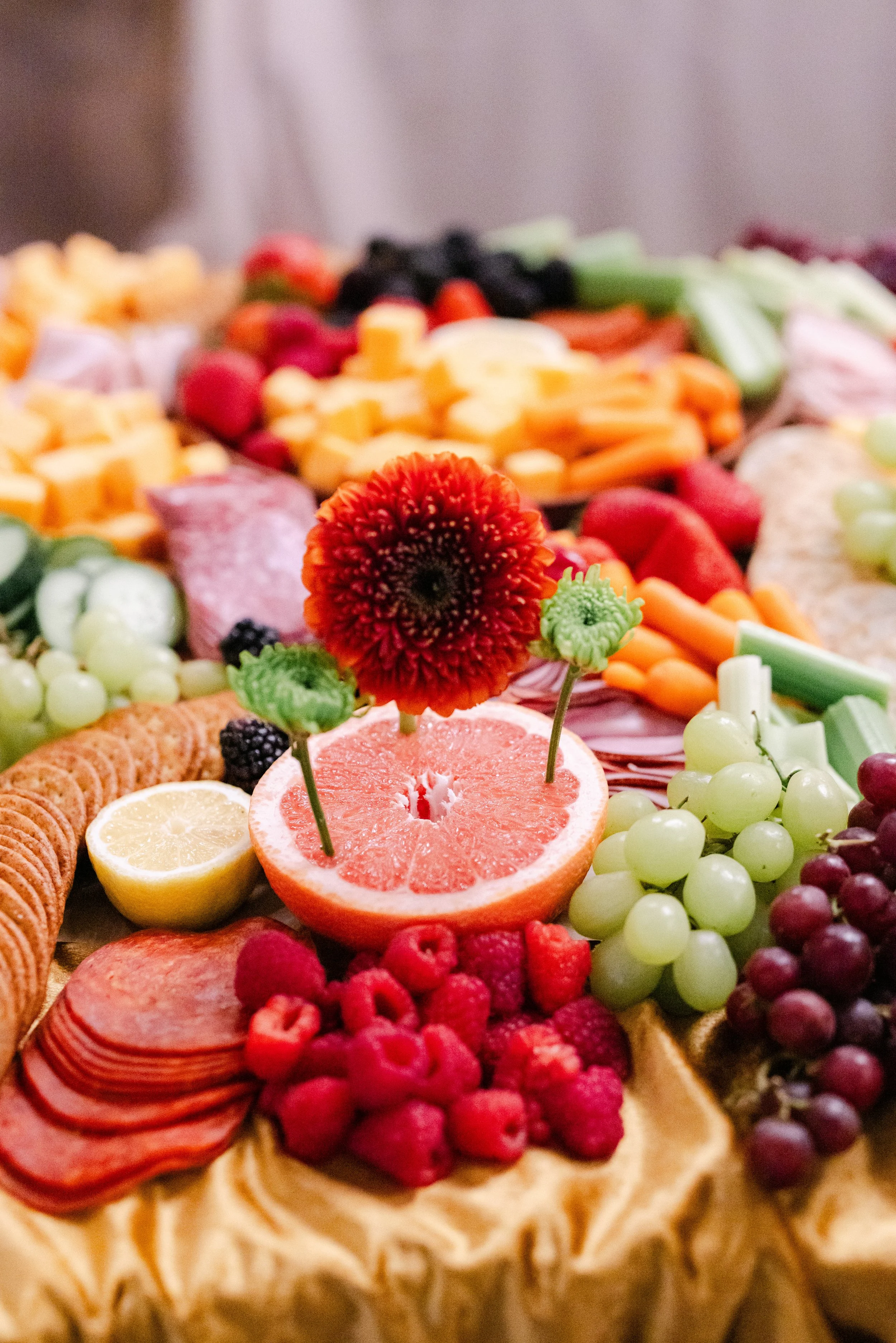 A fruit platter featuring grapefruit halves, green and purple grapes, raspberries, blueberries, blackberries, and slices of lemon, with various cheeses and crackers.