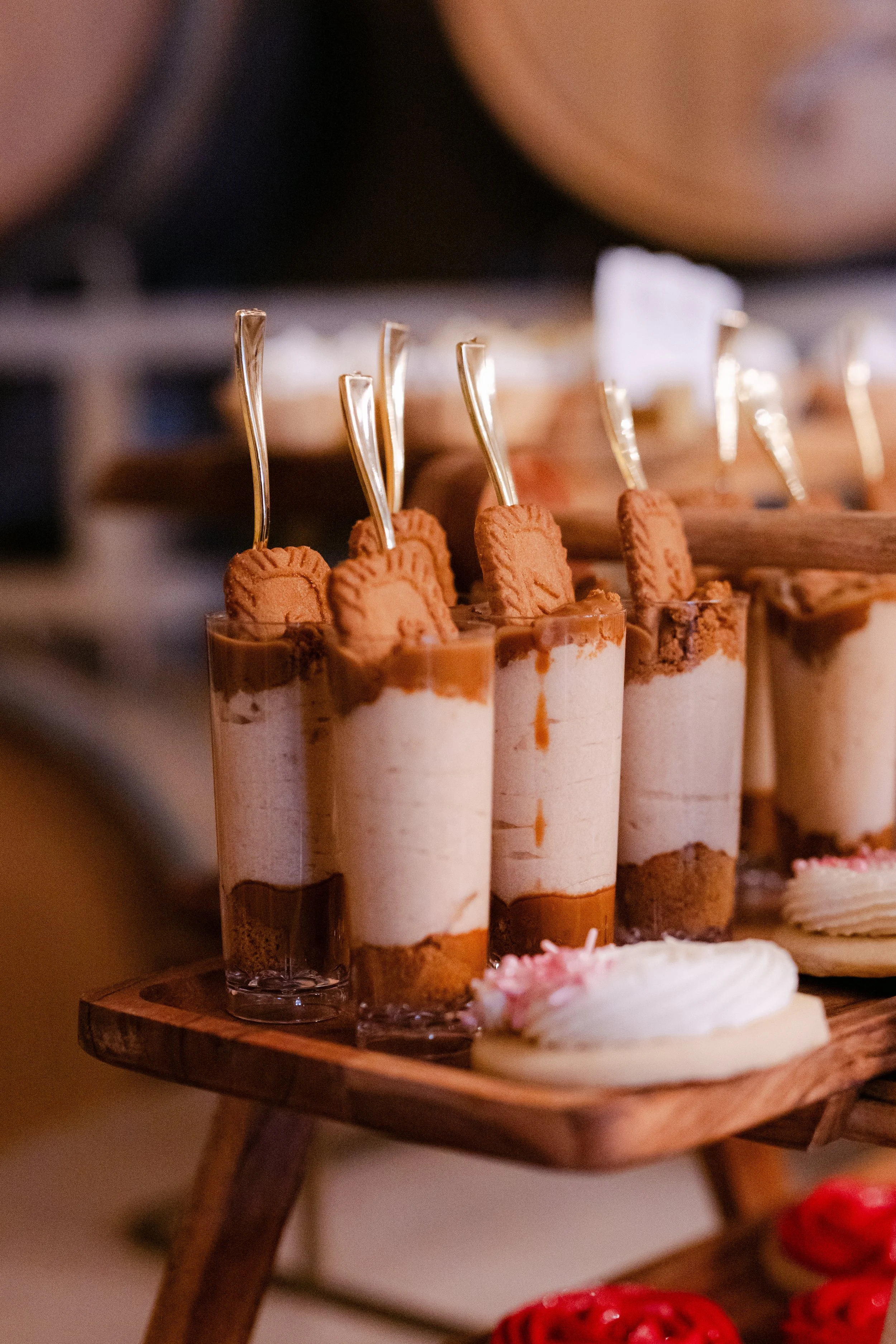 Close-up of several dessert parfaits with cookies and ice cream in tall glasses on a wooden serving tray.