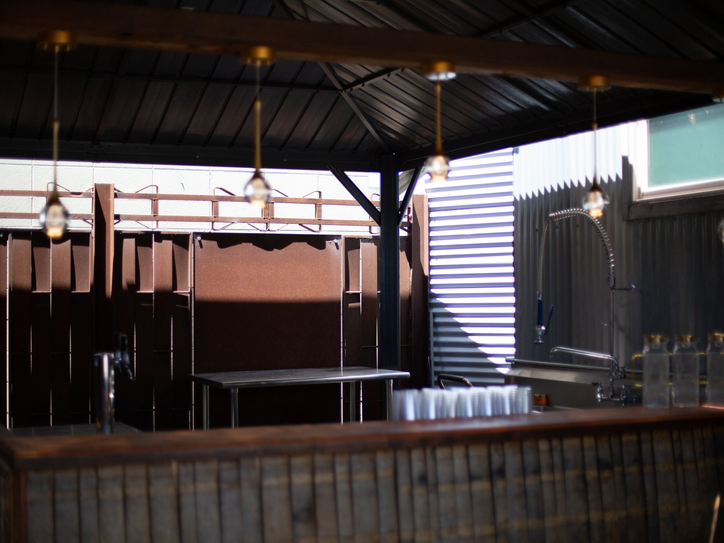 Outdoor kitchen area with dark wooden pergola, string lights, a metal sink with a flexible hose, and a patio in the background.