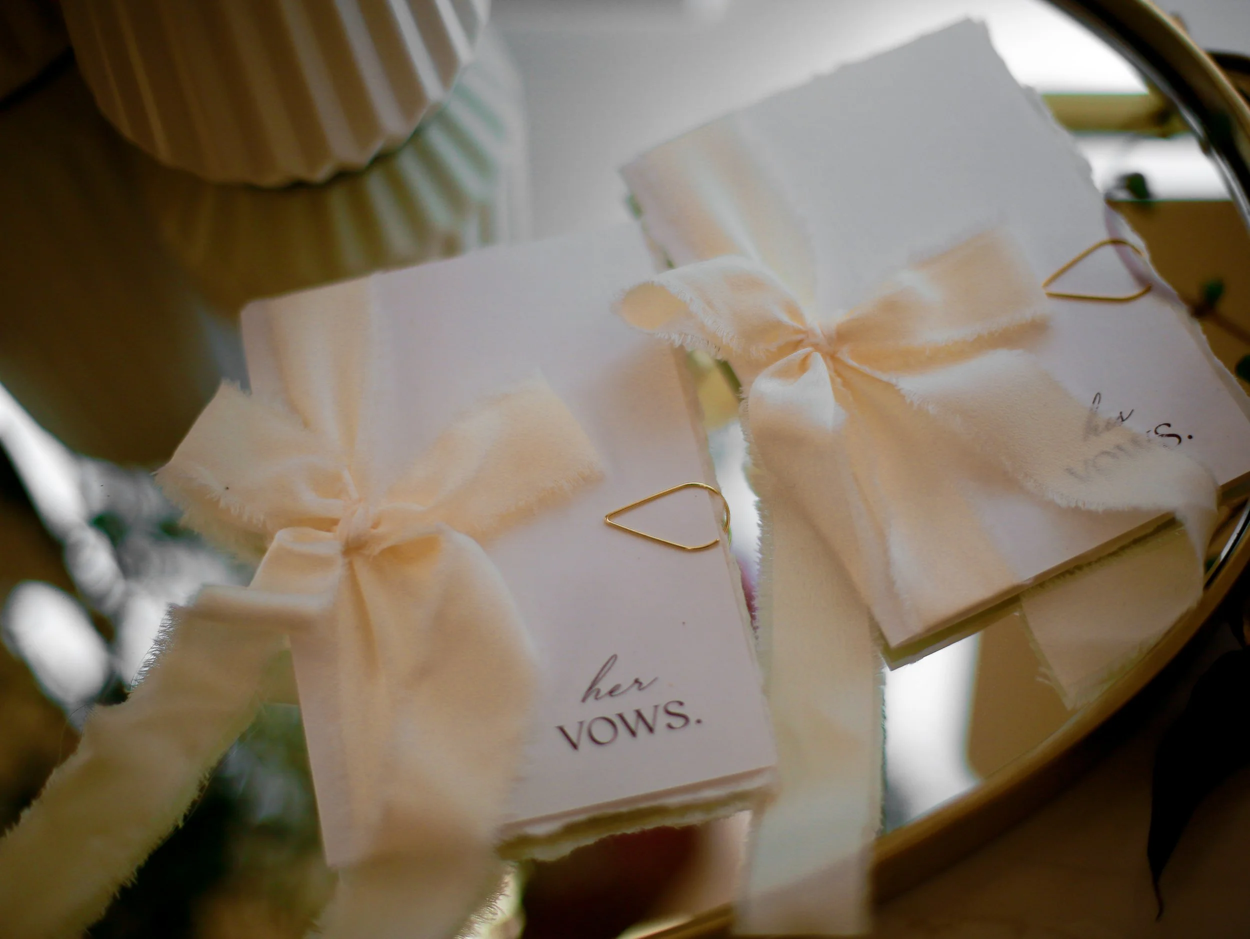 Close-up of a wedding card with a white ribbon and gold clips, placed on a wooden surface.
