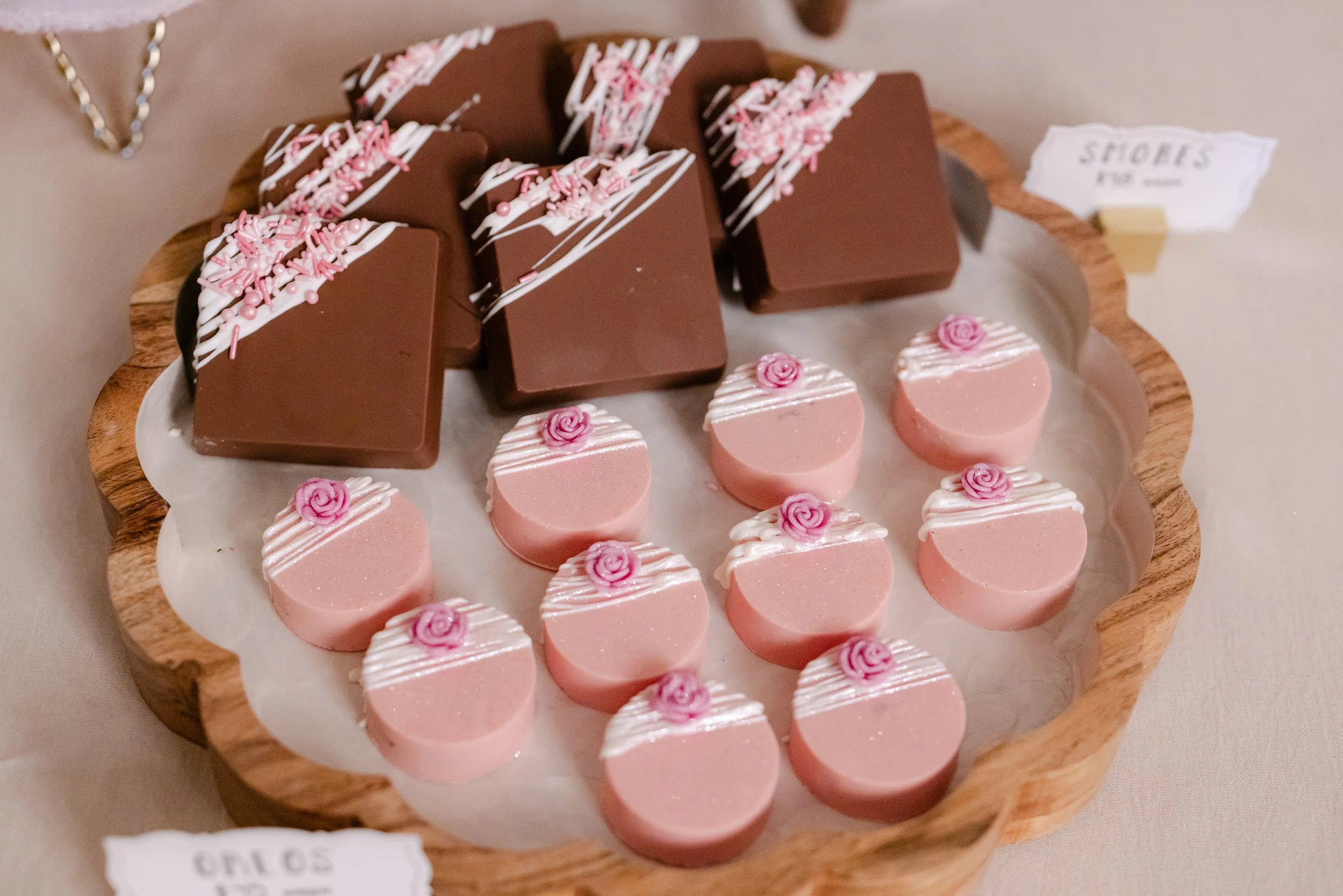 Assorted pink and brown desserts on a wooden tray, decorated with white icing and pink toppings.