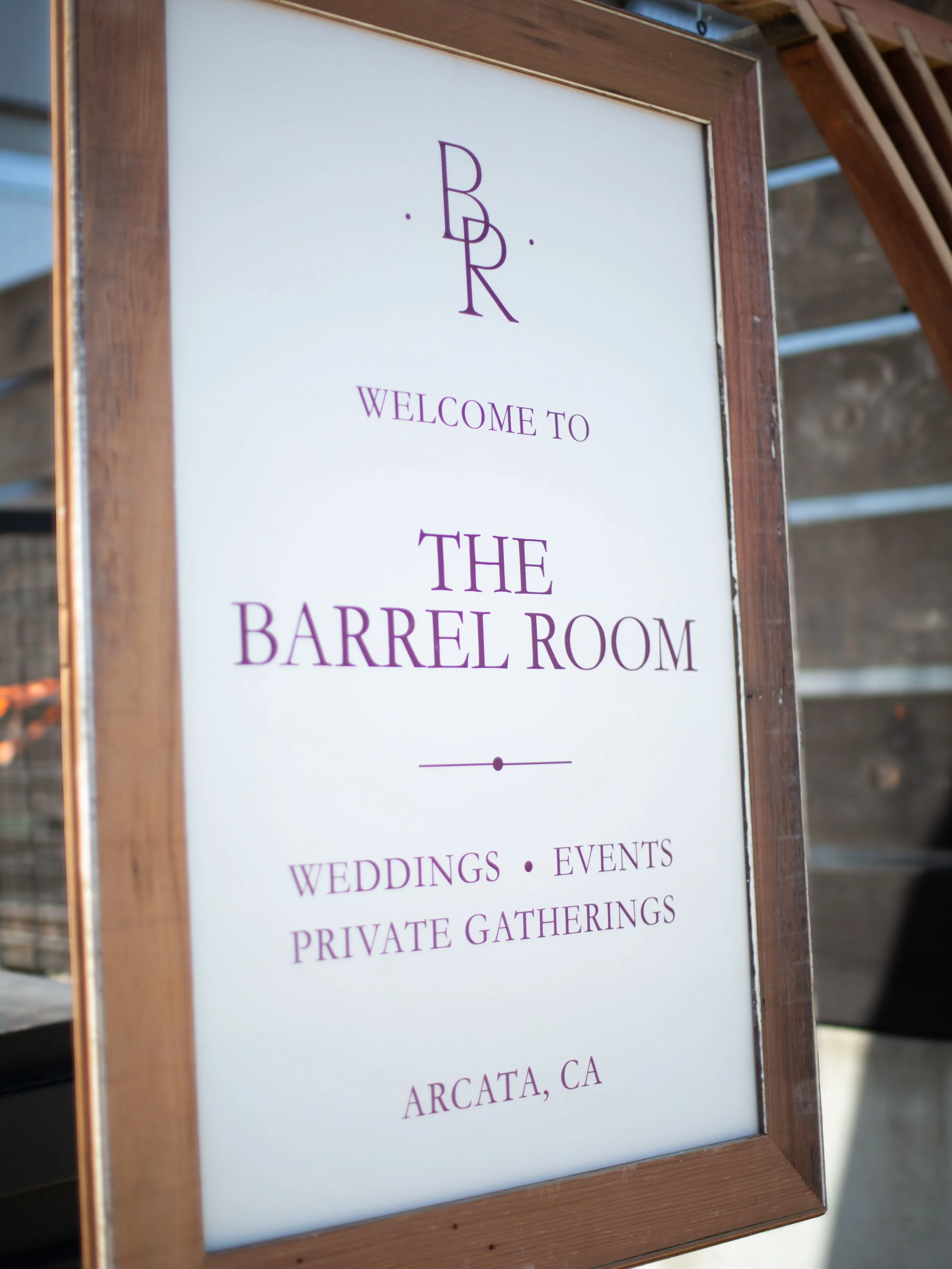 A framed sign with purple text that reads "Welcome to The Barrel Room" and additional details about weddings, events, and private gatherings in Arcata, California.