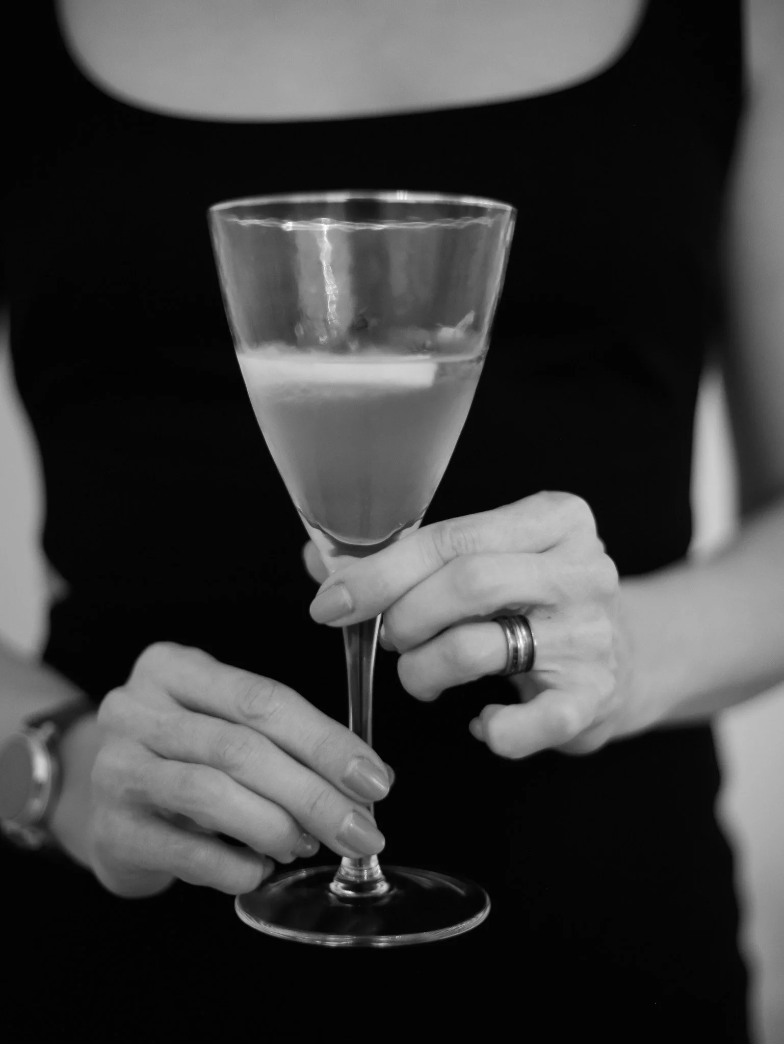 A person holding a wine glass filled with water, focusing on the hand and glass, with a dark background.