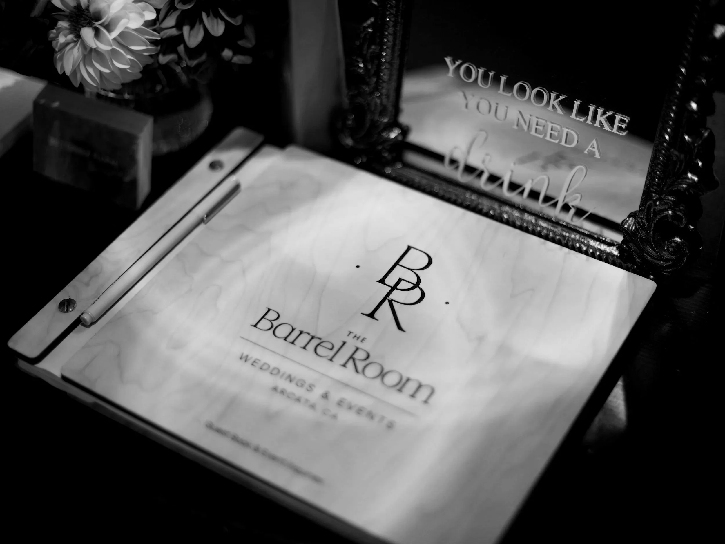 A close-up of wedding event details on paper, with a decorative mirror reading "You Look Like You Need a Hug," and a flower arrangement in the background.