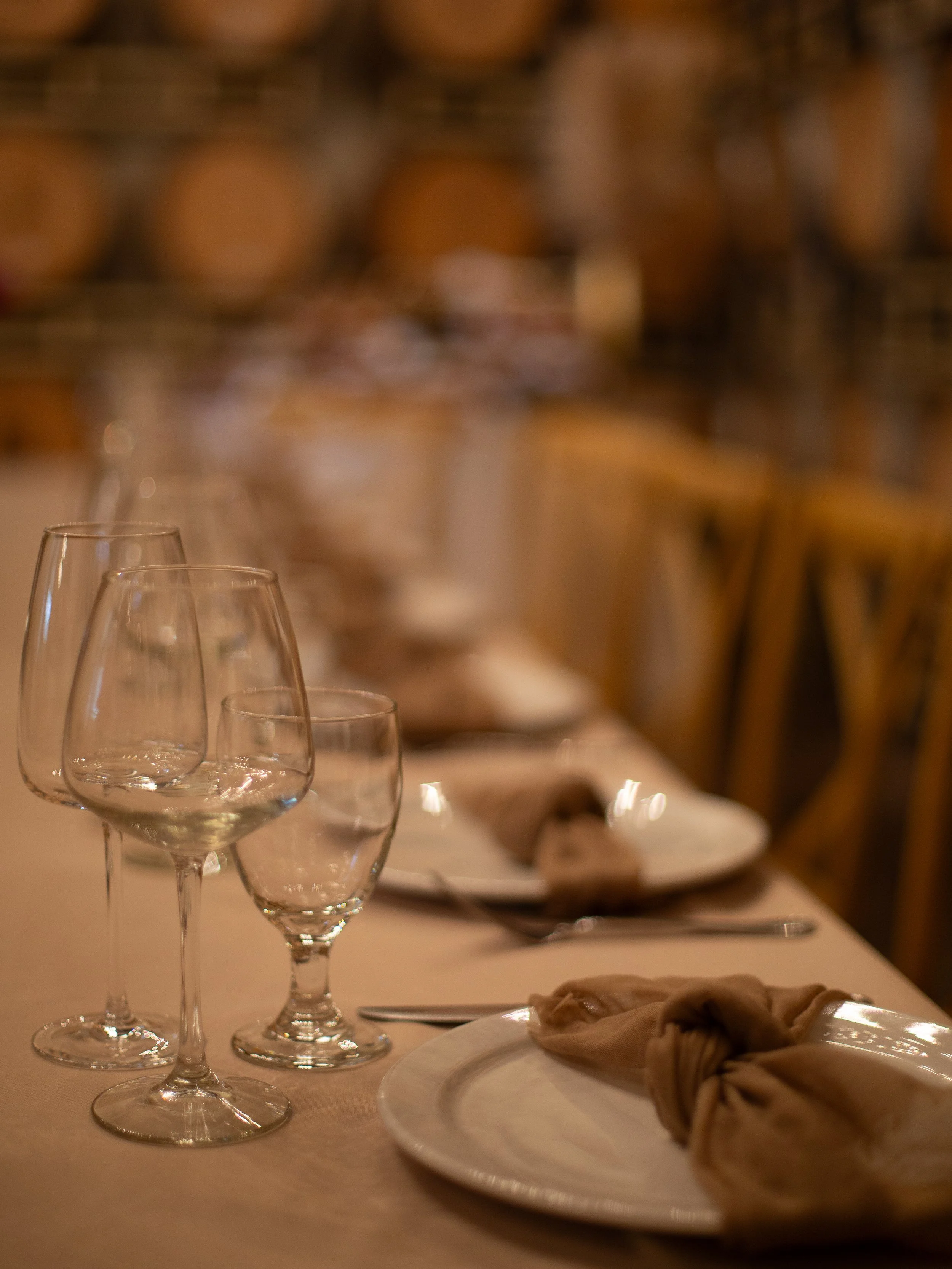 Close-up of empty wine glasses on a dining table with a plate and napkin, blurred background of a restaurant or dining area.