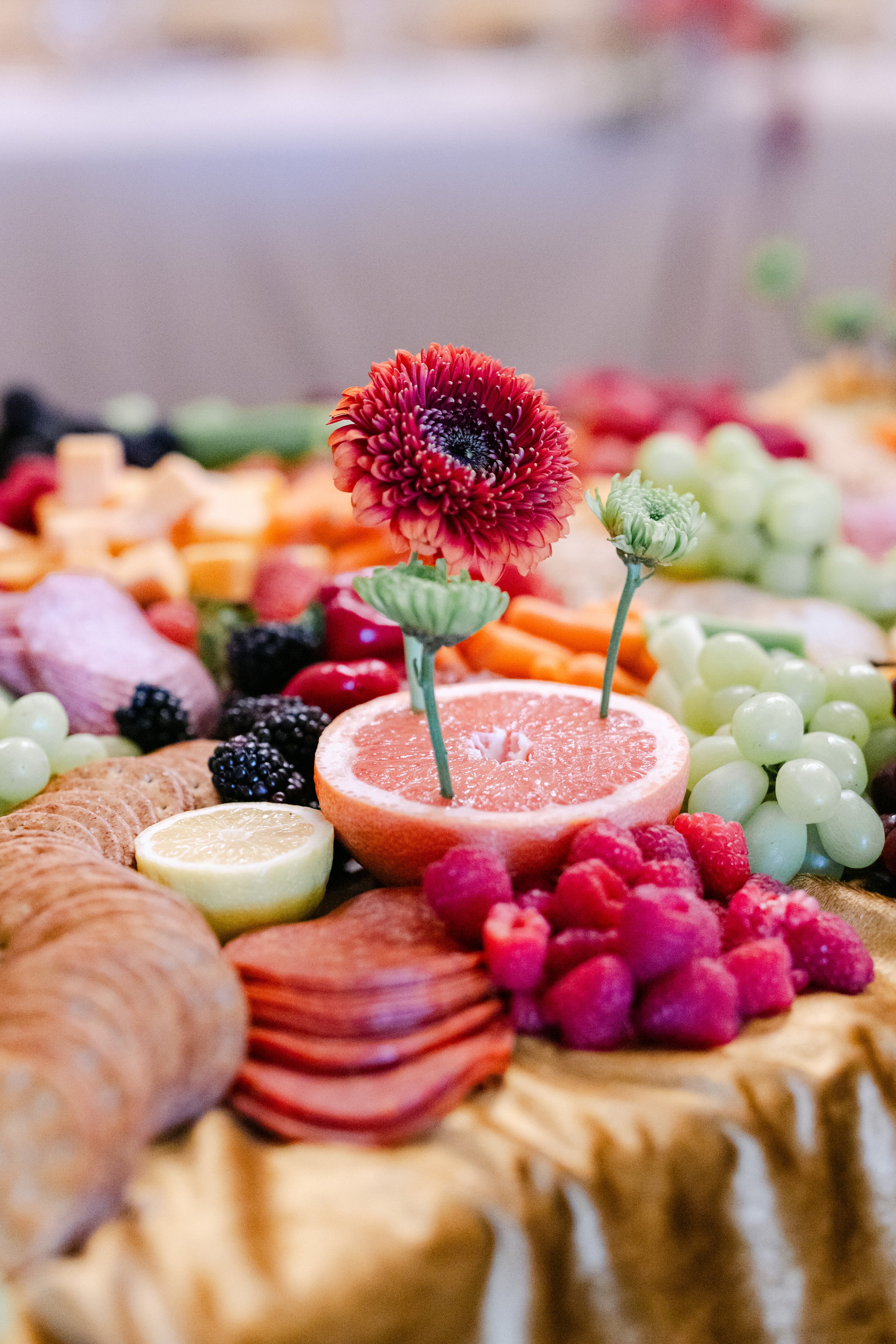 Close-up of a fruit platter featuring a pink and purple flower, sliced grapefruit, lemon, raspberries, blackberries, grapes, and various other fresh fruits.