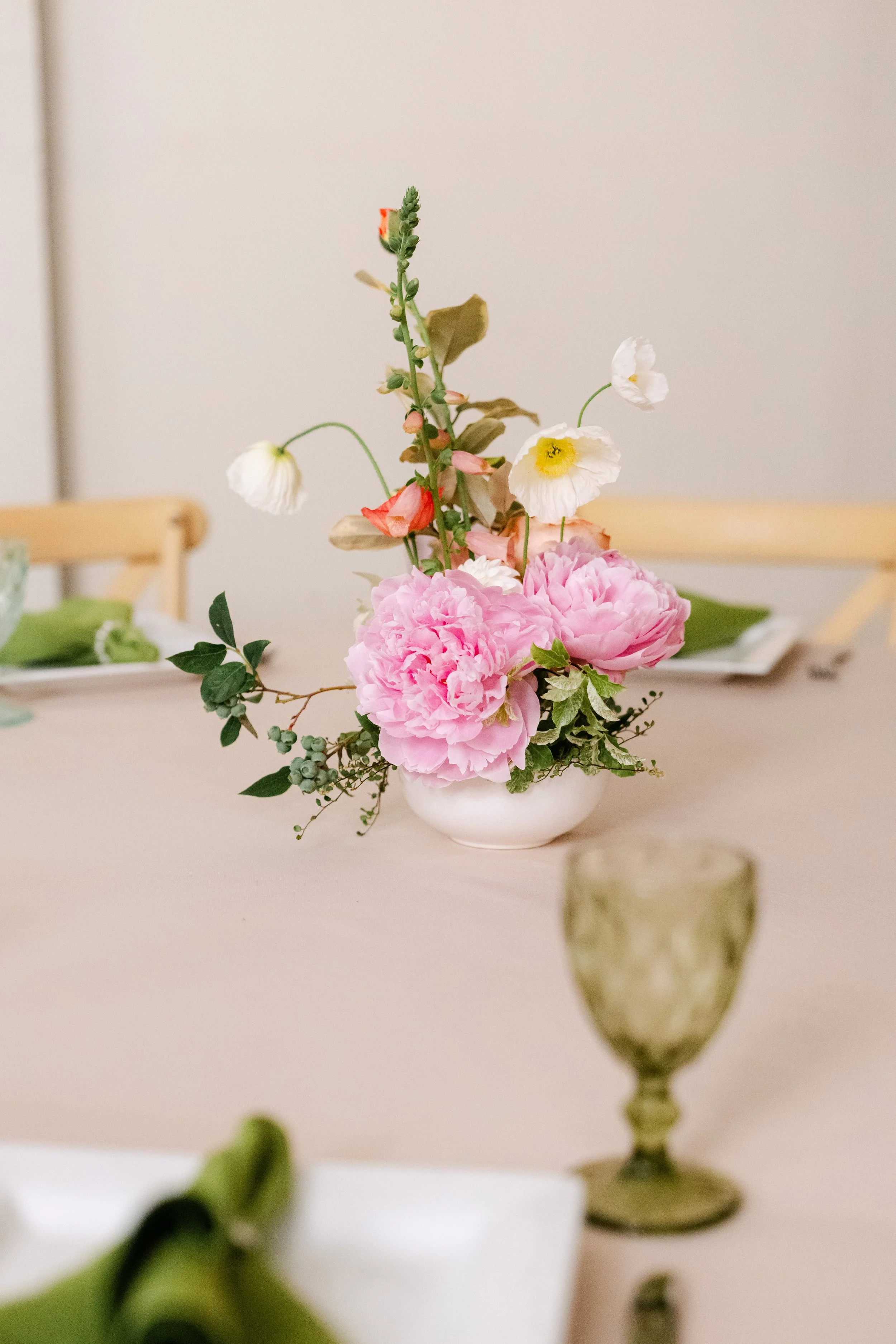 A white vase with pink peonies, white poppies, and greenery on a beige table.