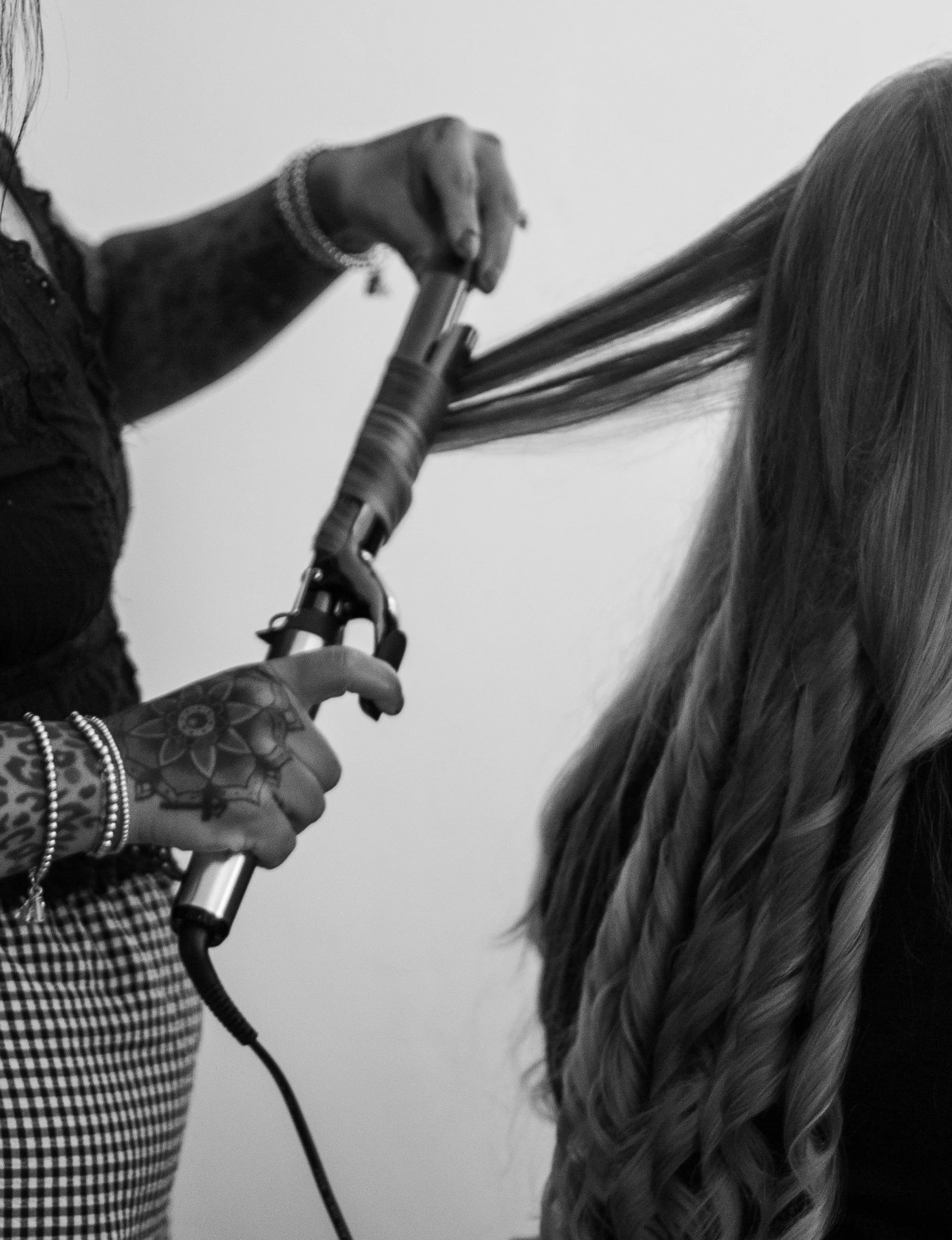 A person is holding a curling iron and styling a woman's long hair, with only the hair and hands visible in the image.