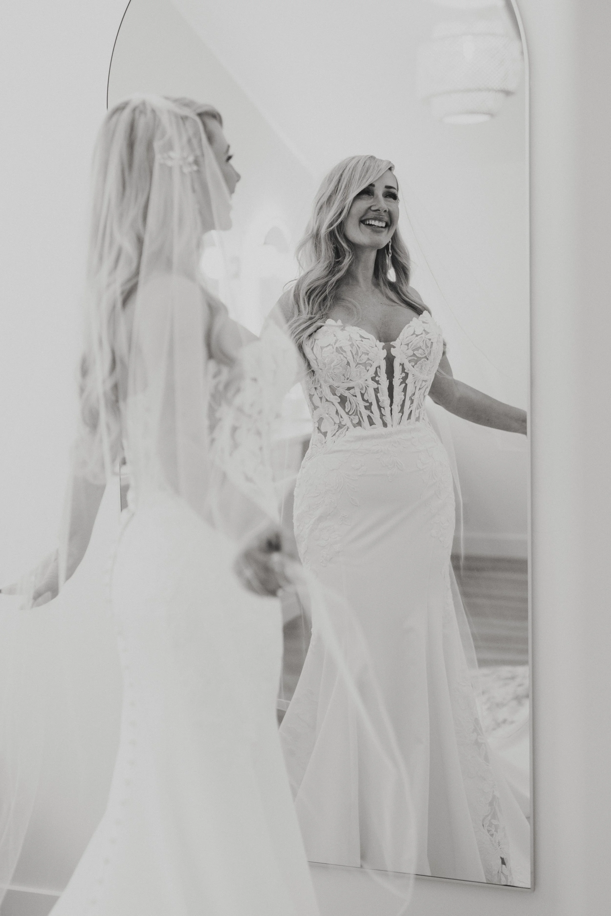 A woman in a wedding dress smiling at her reflection in a mirror.