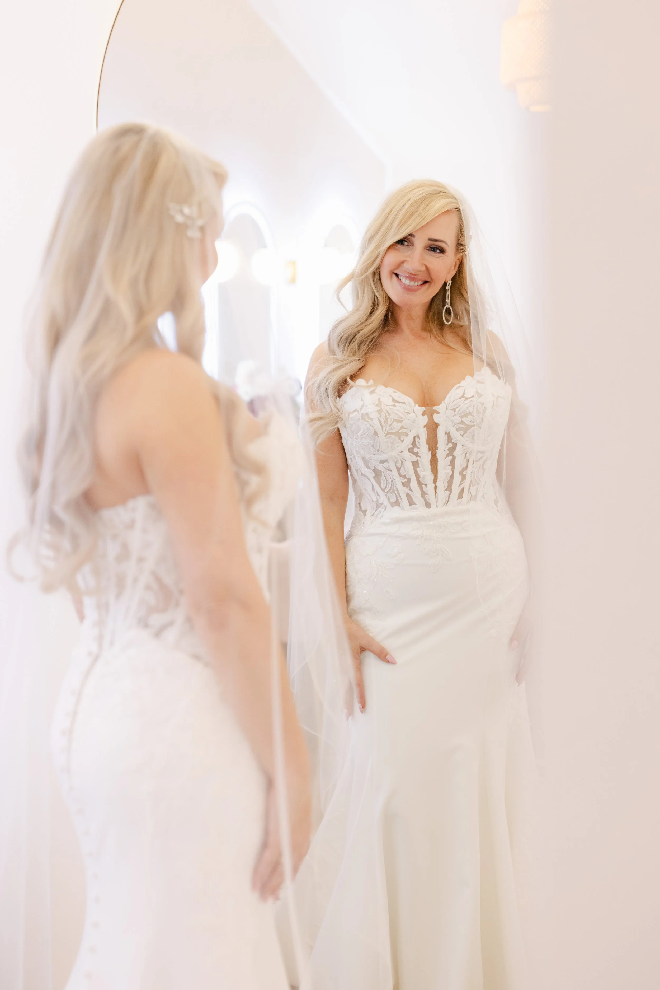 A woman in a wedding dress smiling at her reflection in a mirror.