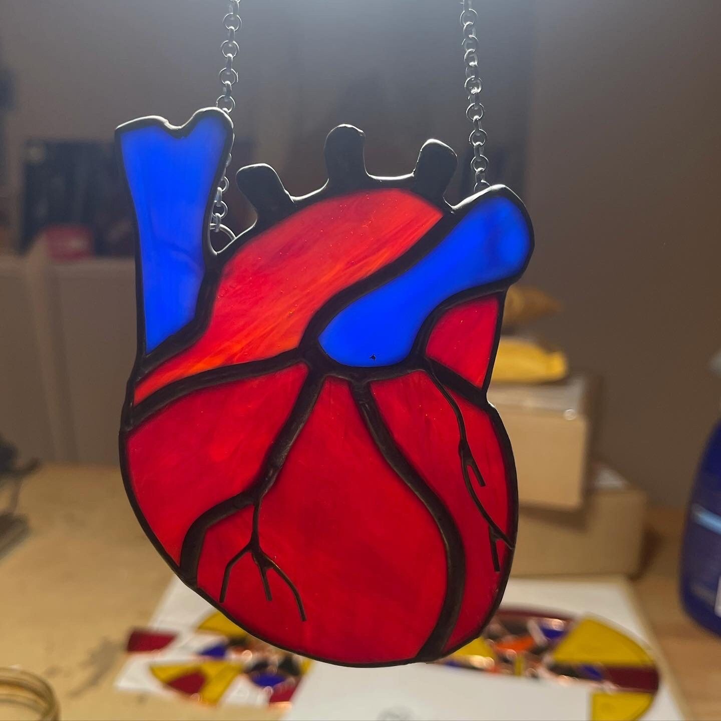 Stained glass heart with red and blue colors and black outlines, hanging from two chains.