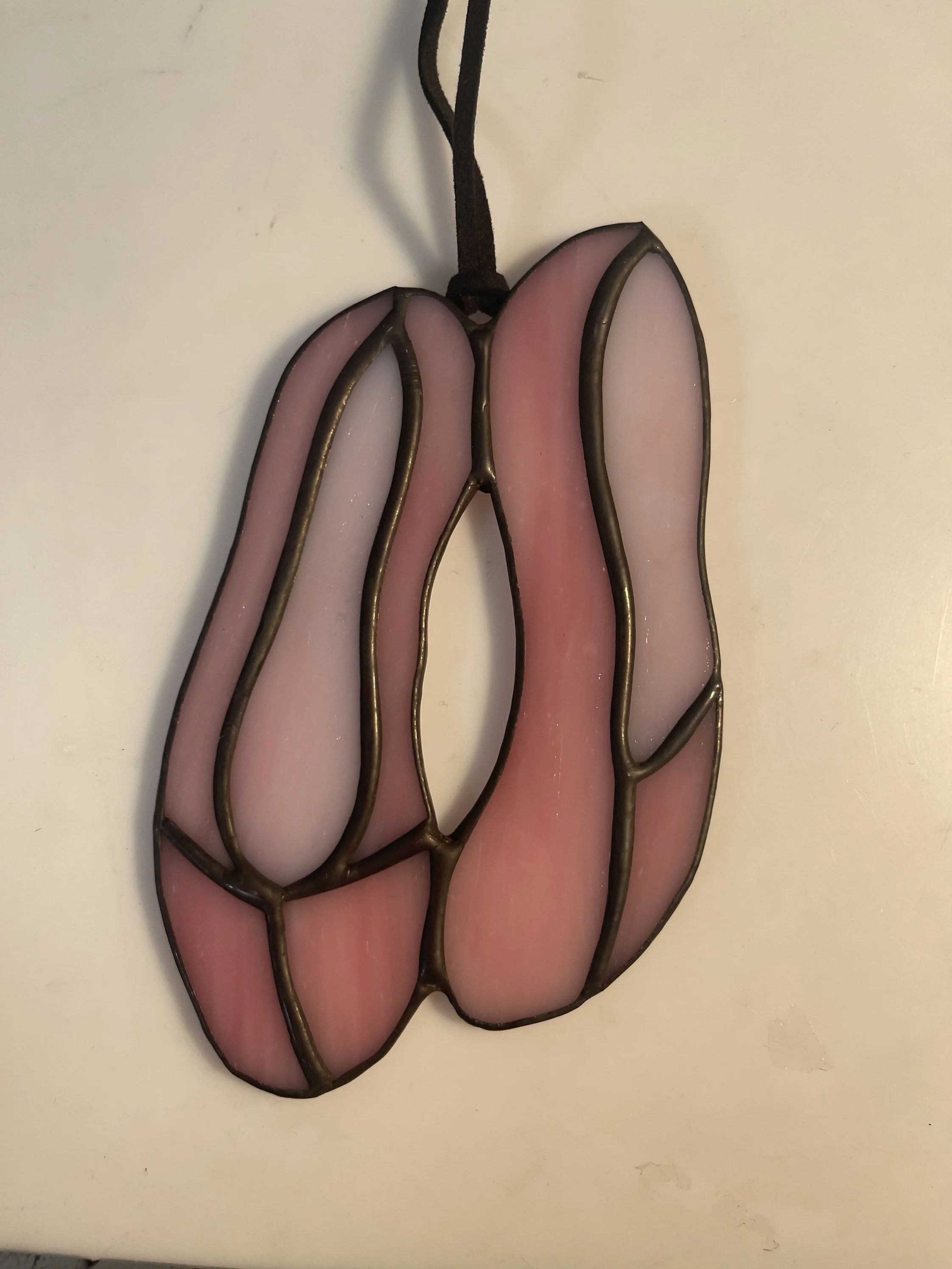 Decorative stained glass wall hanging in the shape of a tulip flower, with pink and white petals and a dark metal frame and black ribbon for hanging.